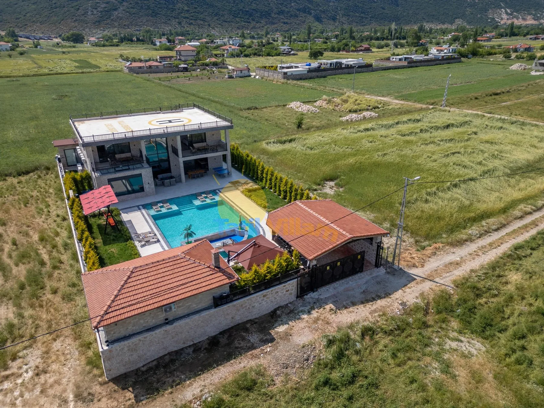 Aerial view of a modern property with a swimming pool amid open fields.