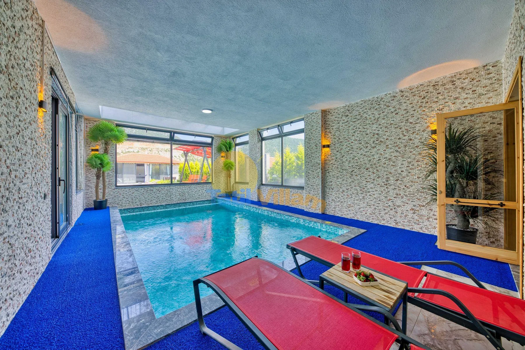 An indoor swimming pool with blue flooring and red lounge chairs.