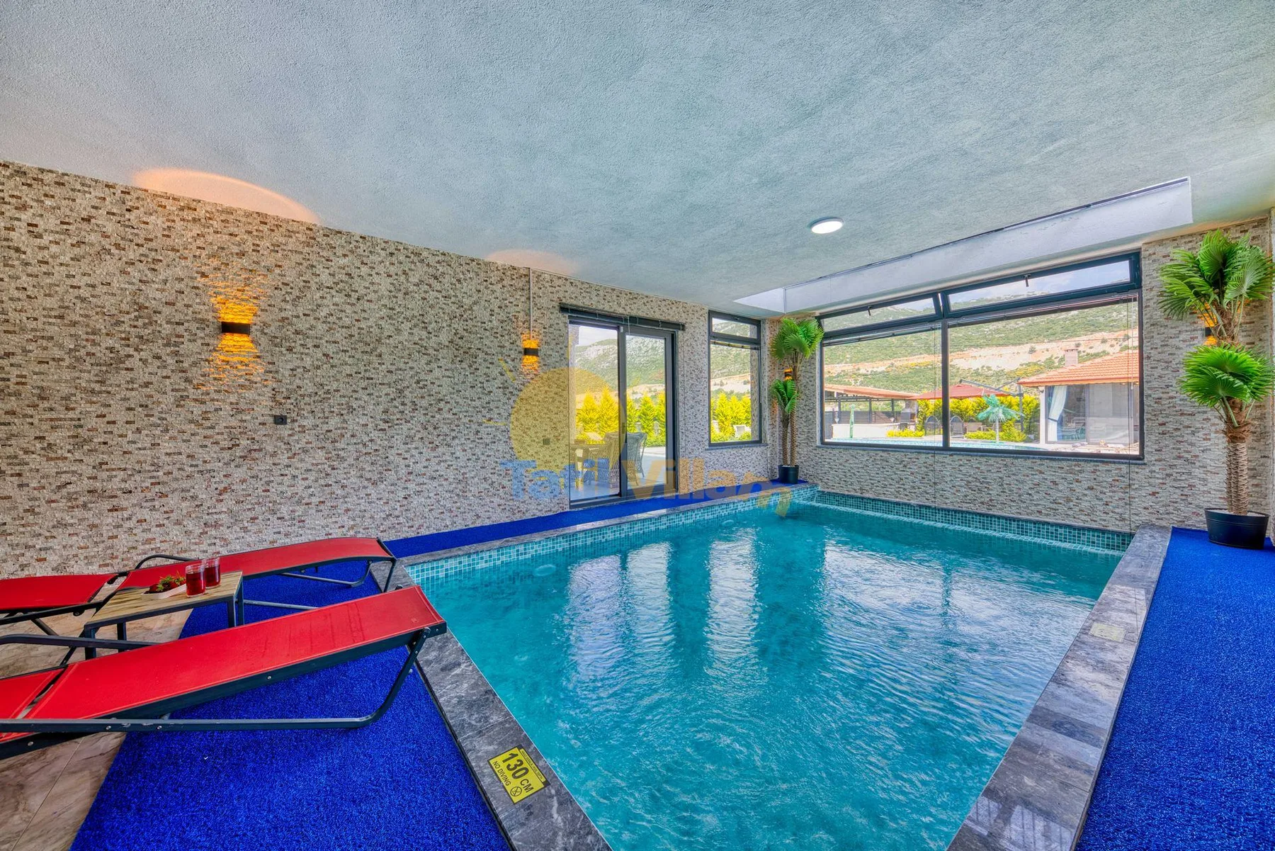 An indoor swimming pool beside large windows and blue deck flooring.