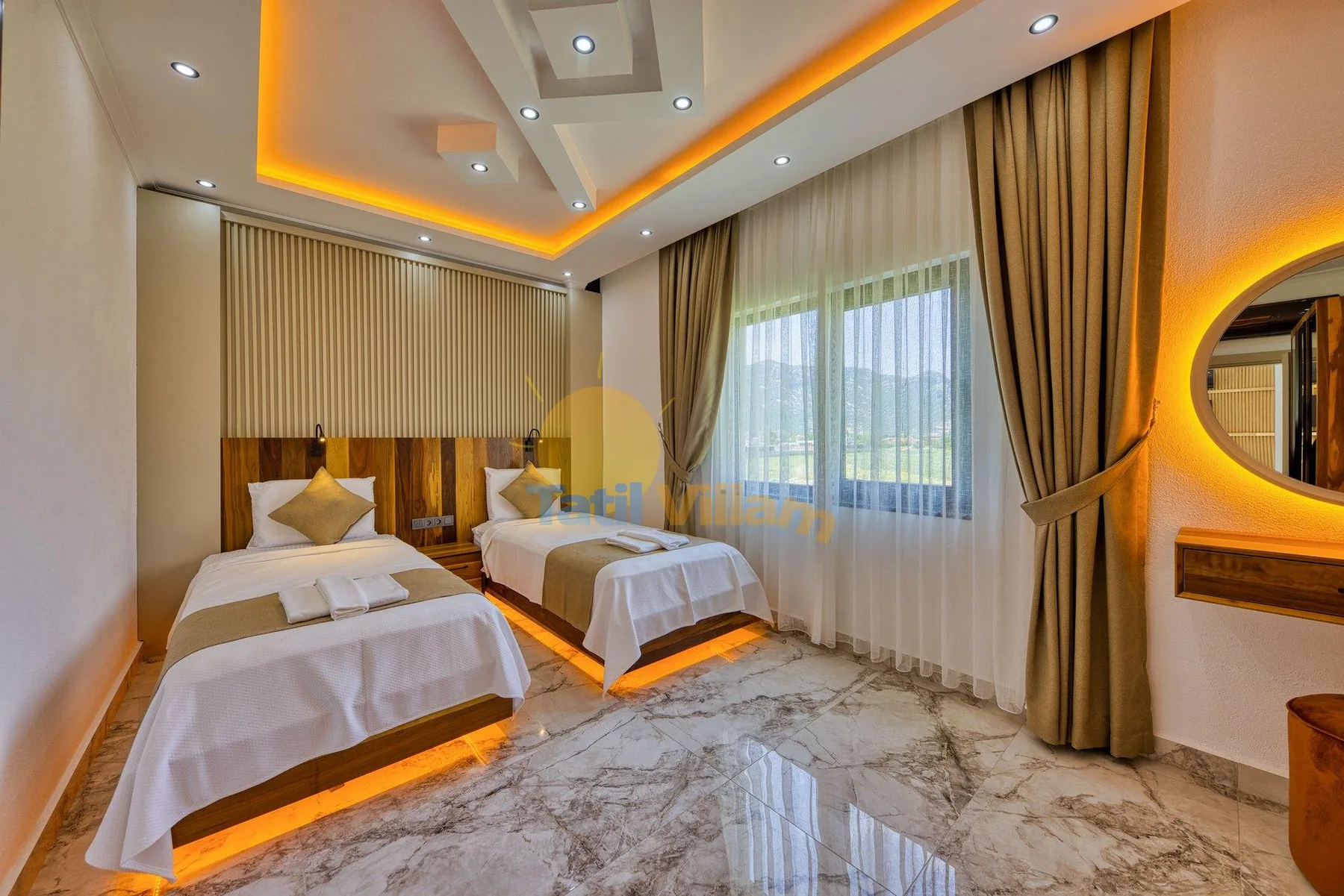 A bedroom with two beds, large curtained windows, and recessed ceiling lighting.