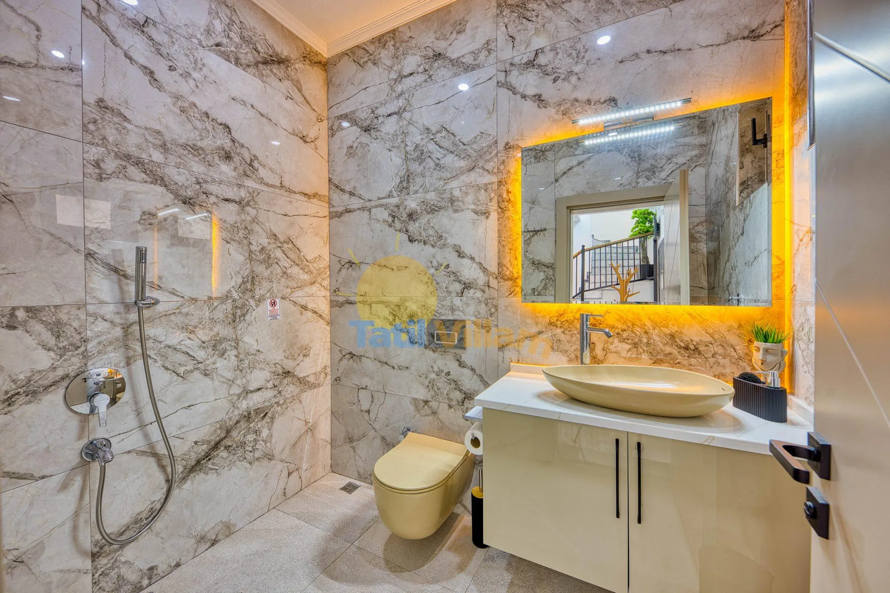 A marble-tiled bathroom with a shower, toilet, and vanity beneath an illuminated mirror.