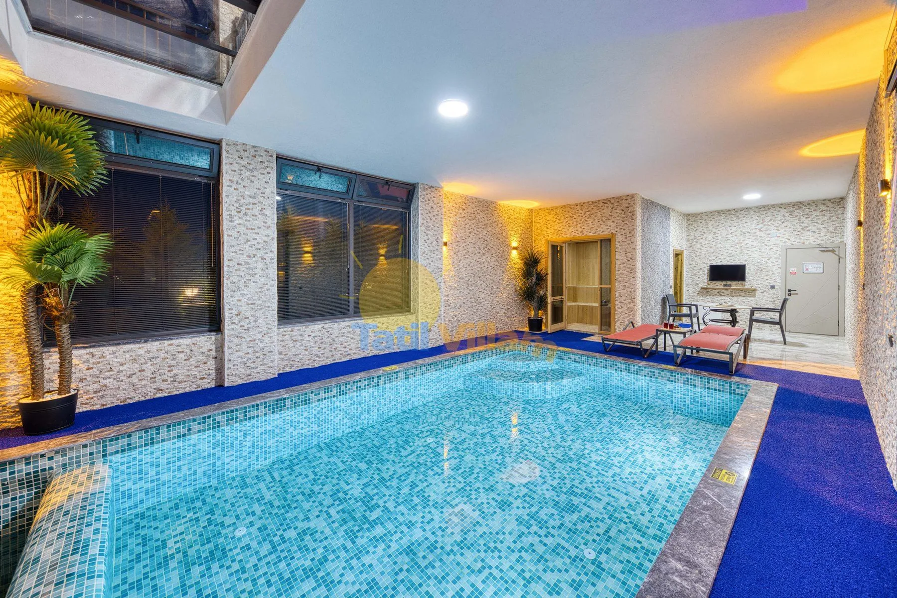 An indoor swimming pool fills the foreground, with seating along the far side.