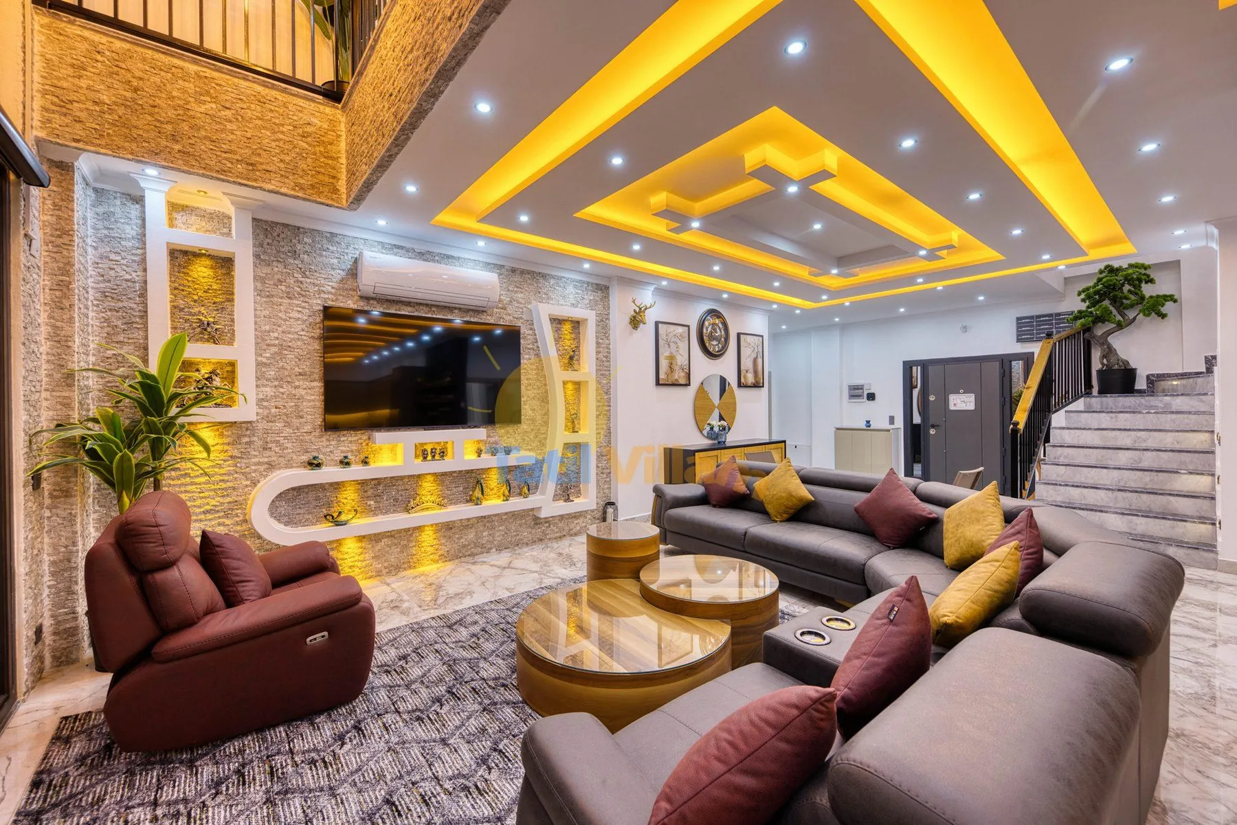 A living room with sectional seating, a television, and a staircase.