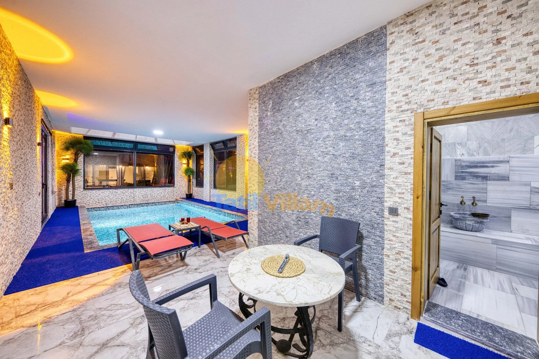 Indoor pool area with a round table and seating in the foreground.