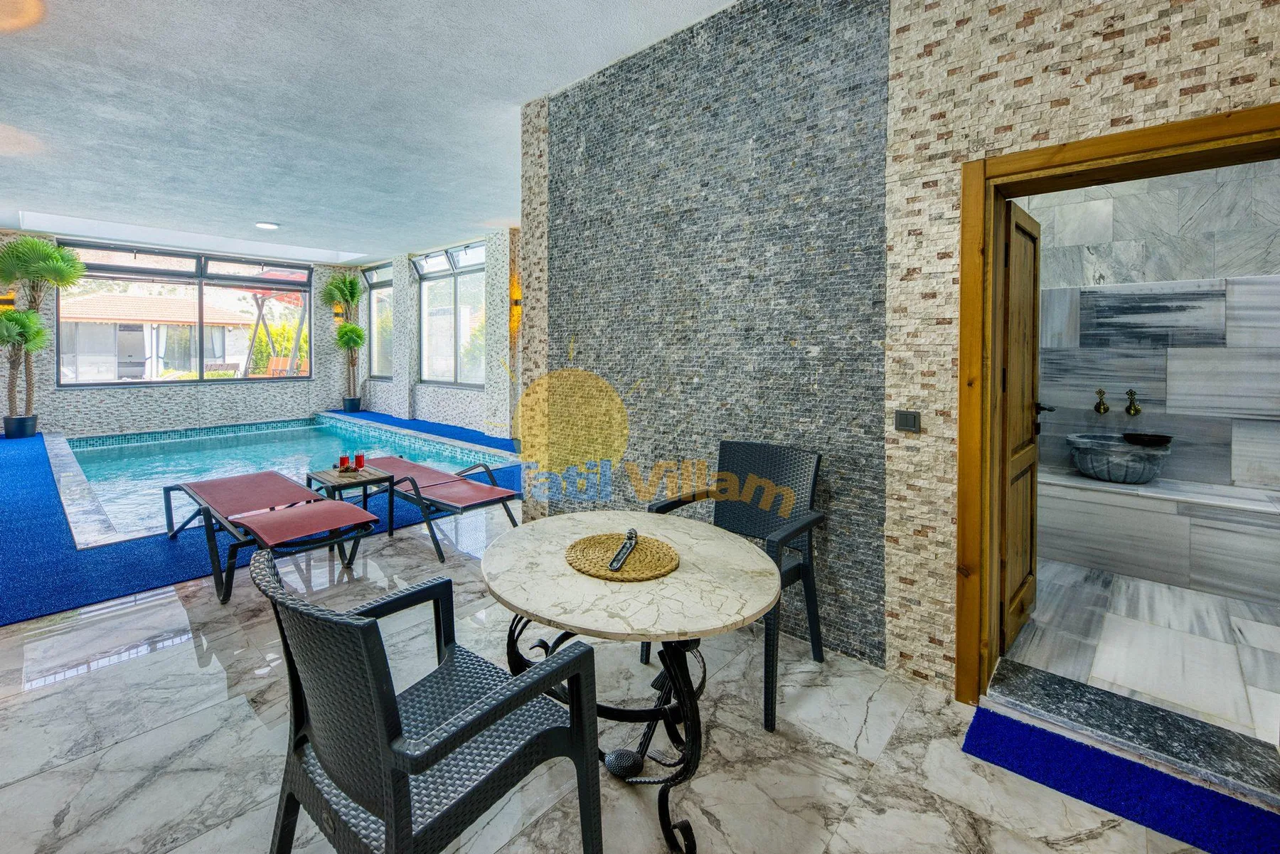 A tiled indoor pool area has a round table and seating beside the water.