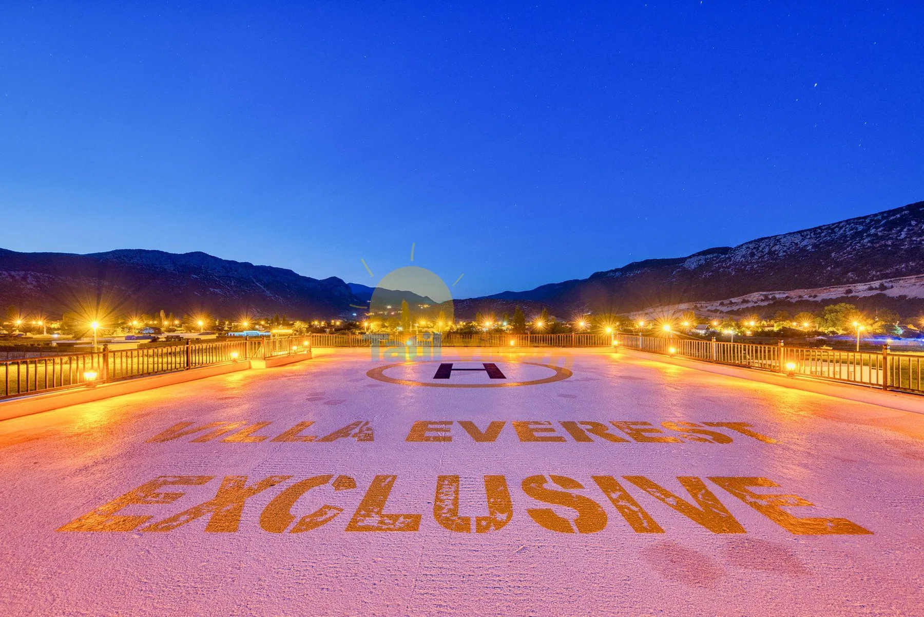 An illuminated outdoor paved area displays large lettering beneath a blue evening sky.