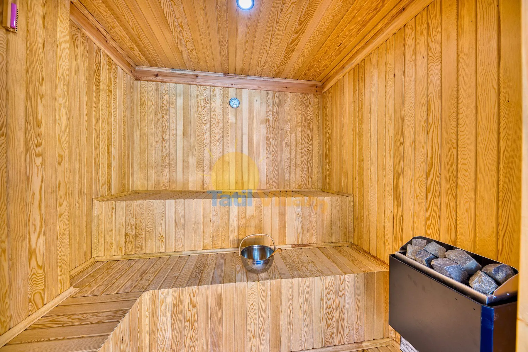 A wood-paneled sauna room with tiered seating and a heater filled with stones.