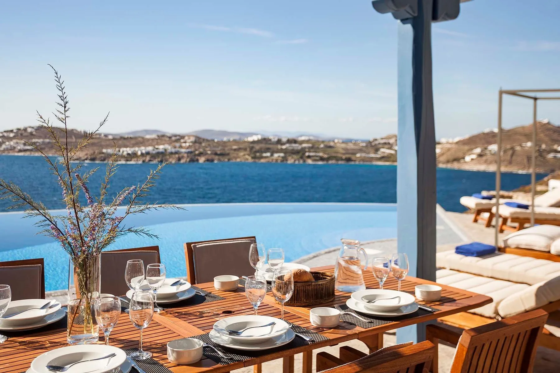 An outdoor dining area overlooks a blue pool and the sea.