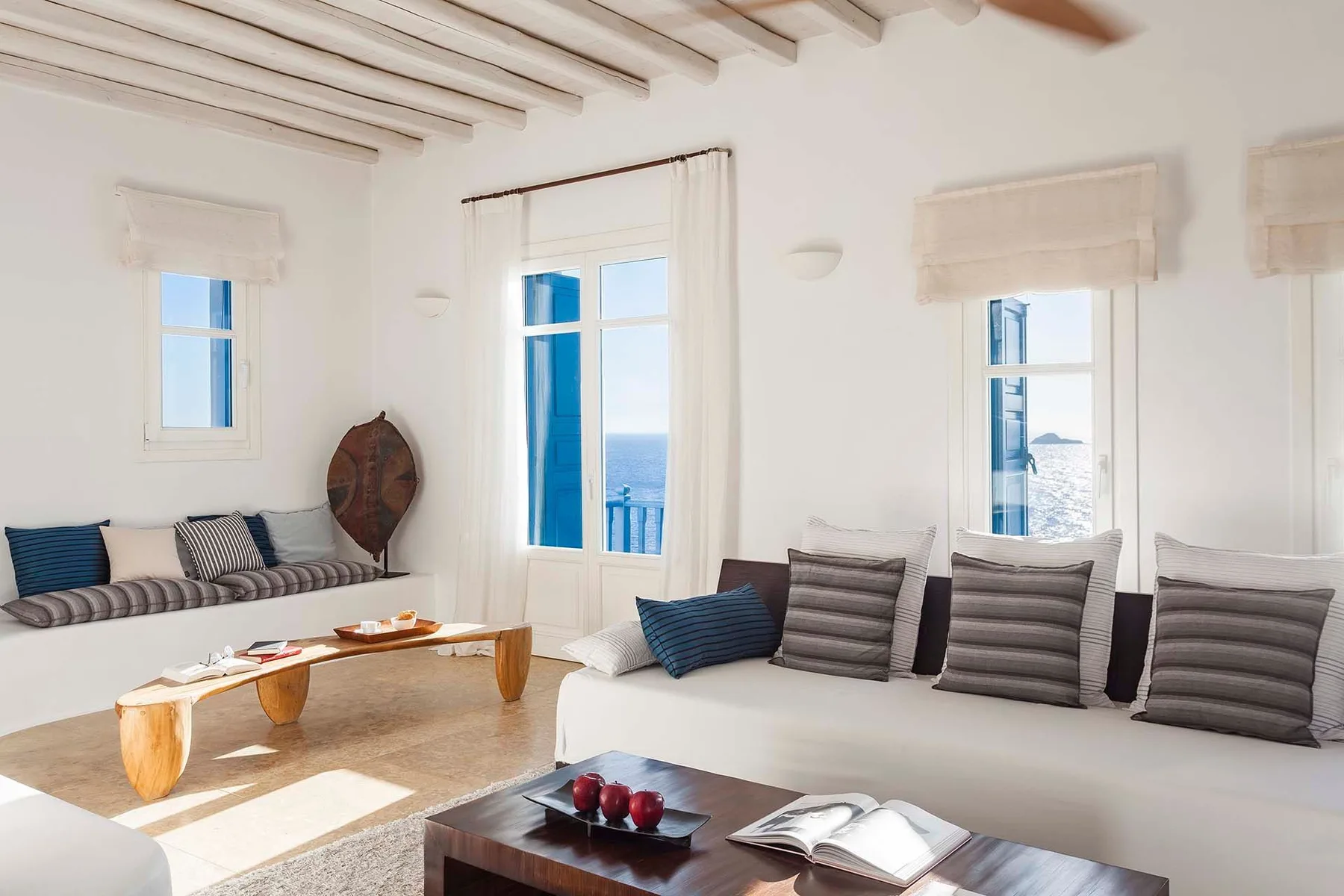 A bright living room with cushioned seating beside large windows overlooking the sea.