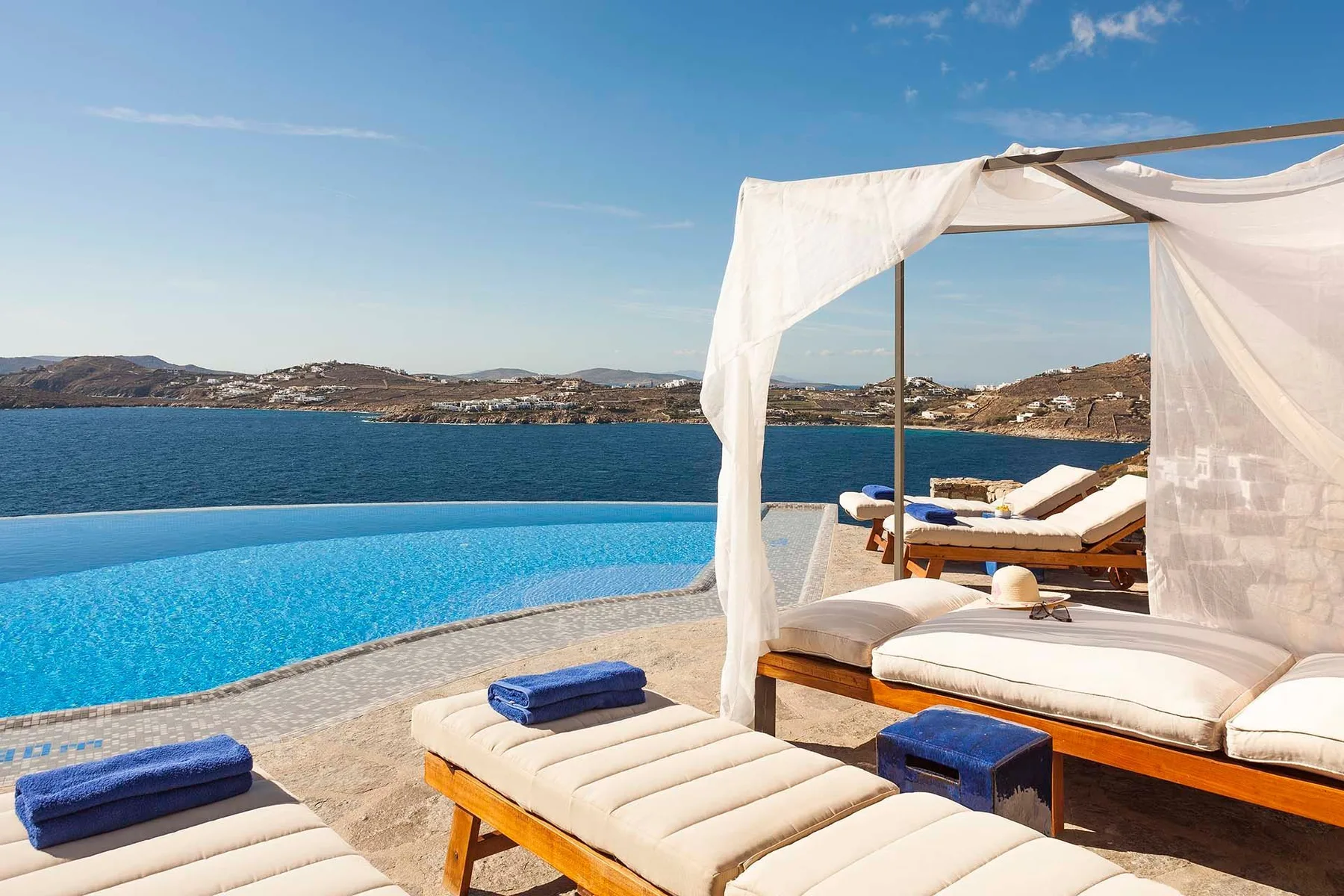 A poolside lounging area overlooks the sea, with cushioned seating beneath a fabric canopy.