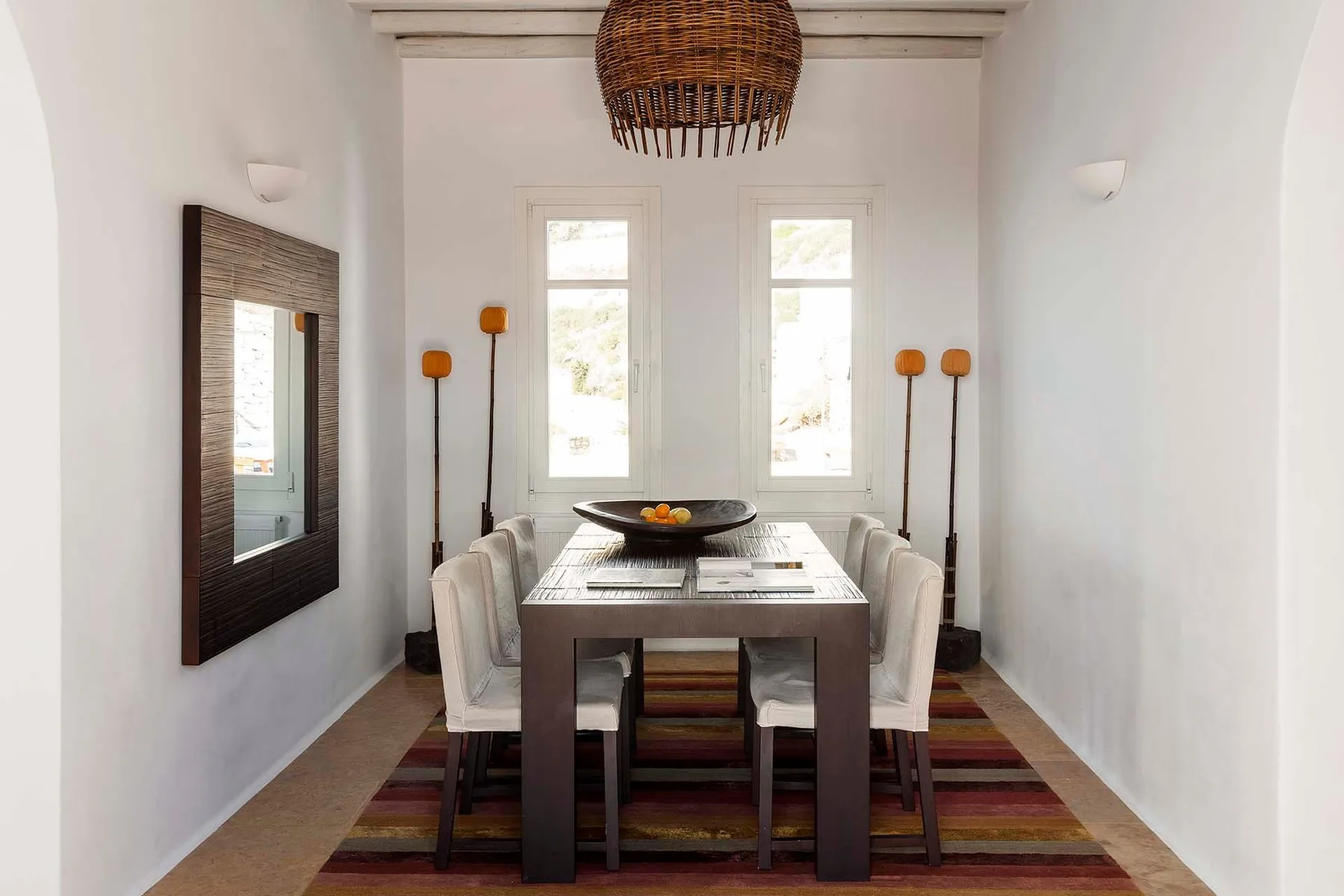A bright dining room with a long table, seating, and two windows.