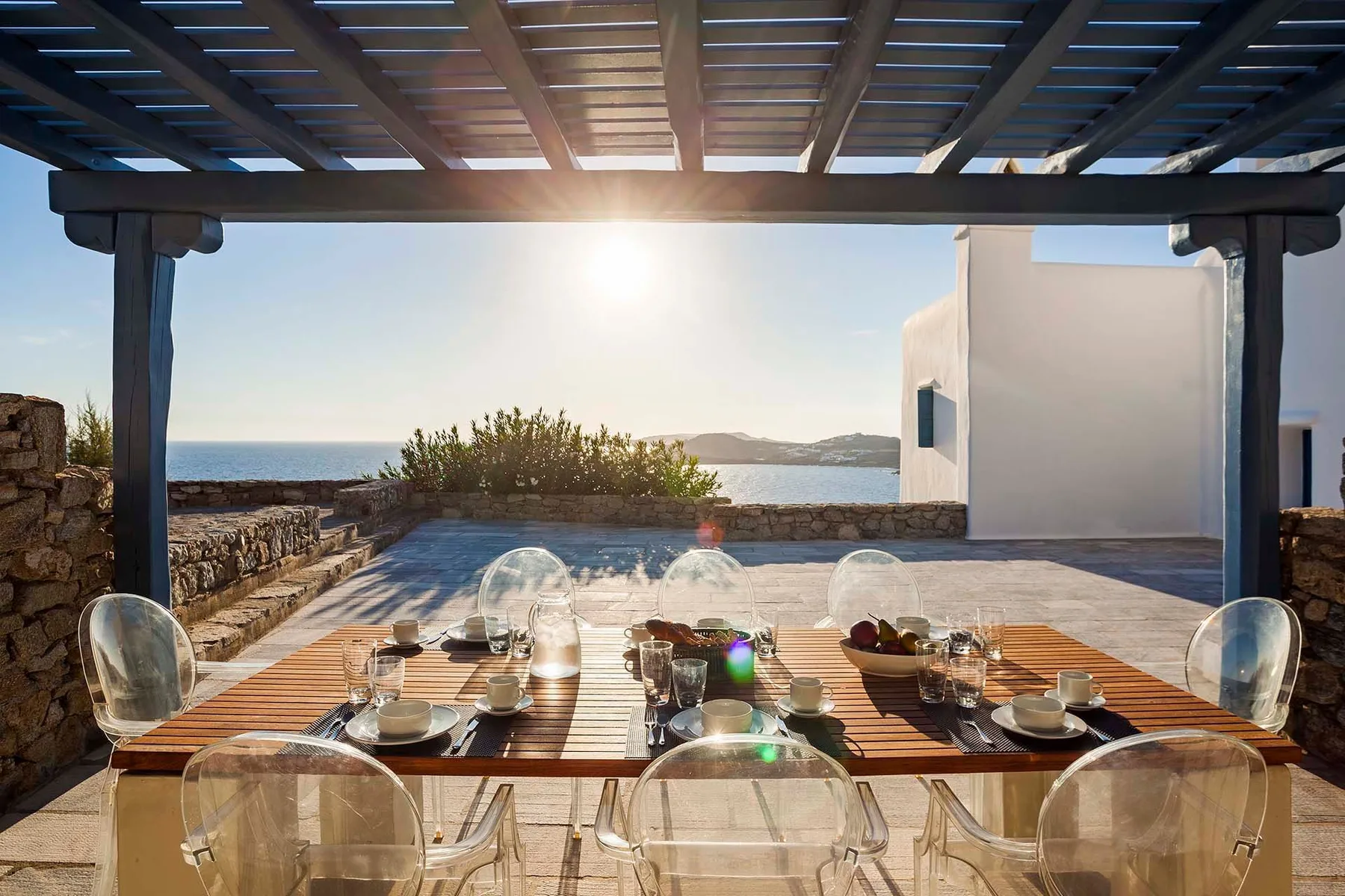 A seaside terrace dining area with a wooden table beneath a pergola.