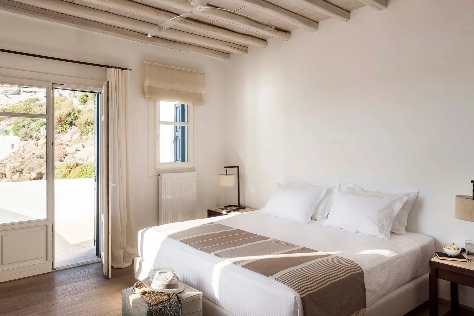 A bright bedroom with a bed, bedside lamps, and a glass door opening onto a terrace.