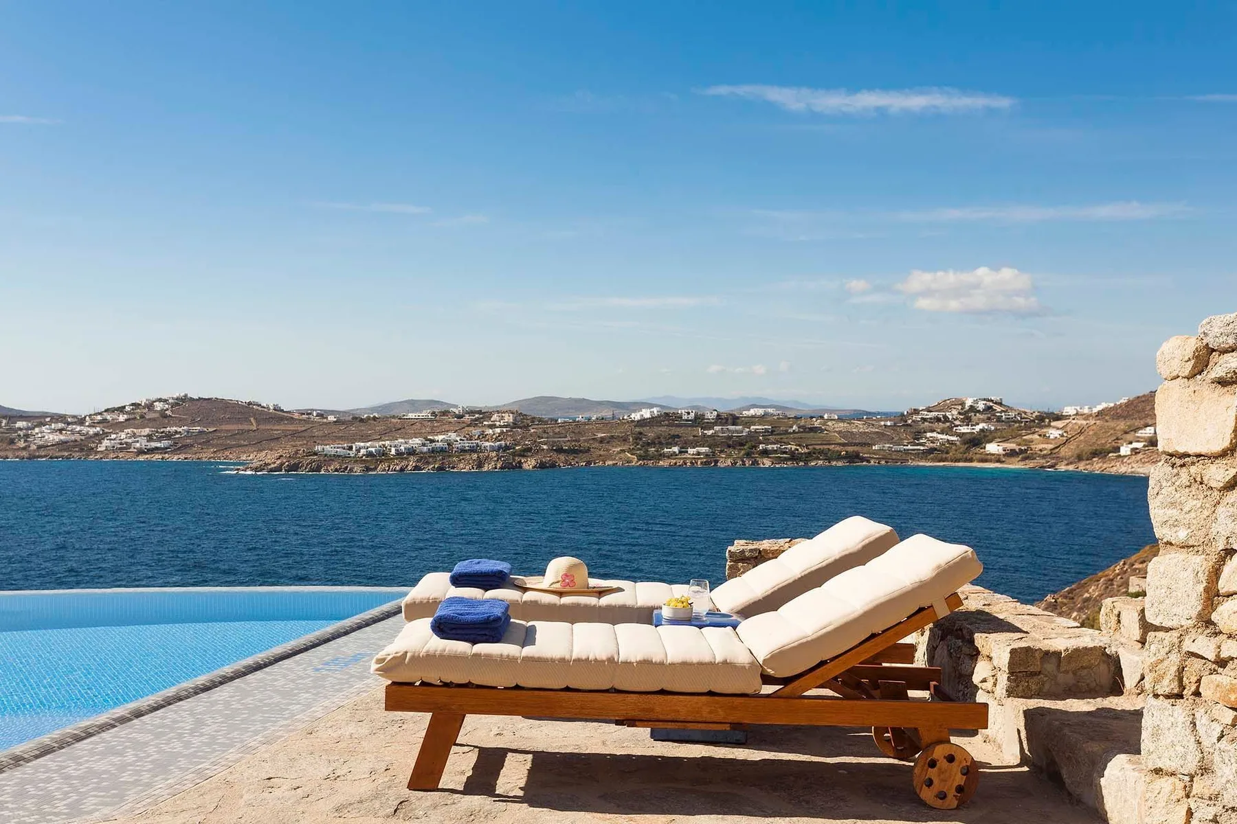 A seaside pool terrace with cushioned loungers overlooking the water.