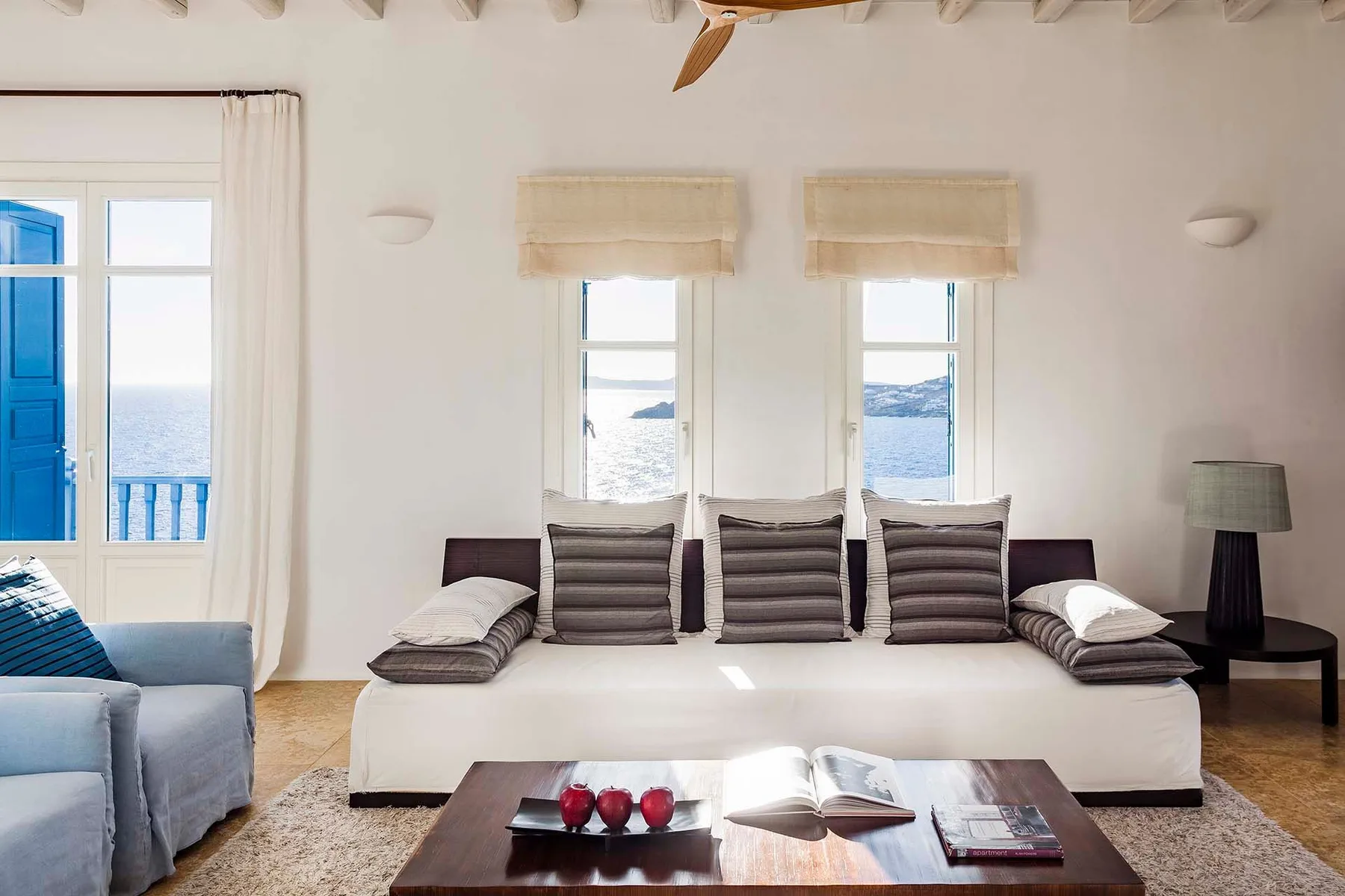 A bright bedroom with a wide bed facing windows overlooking the water.