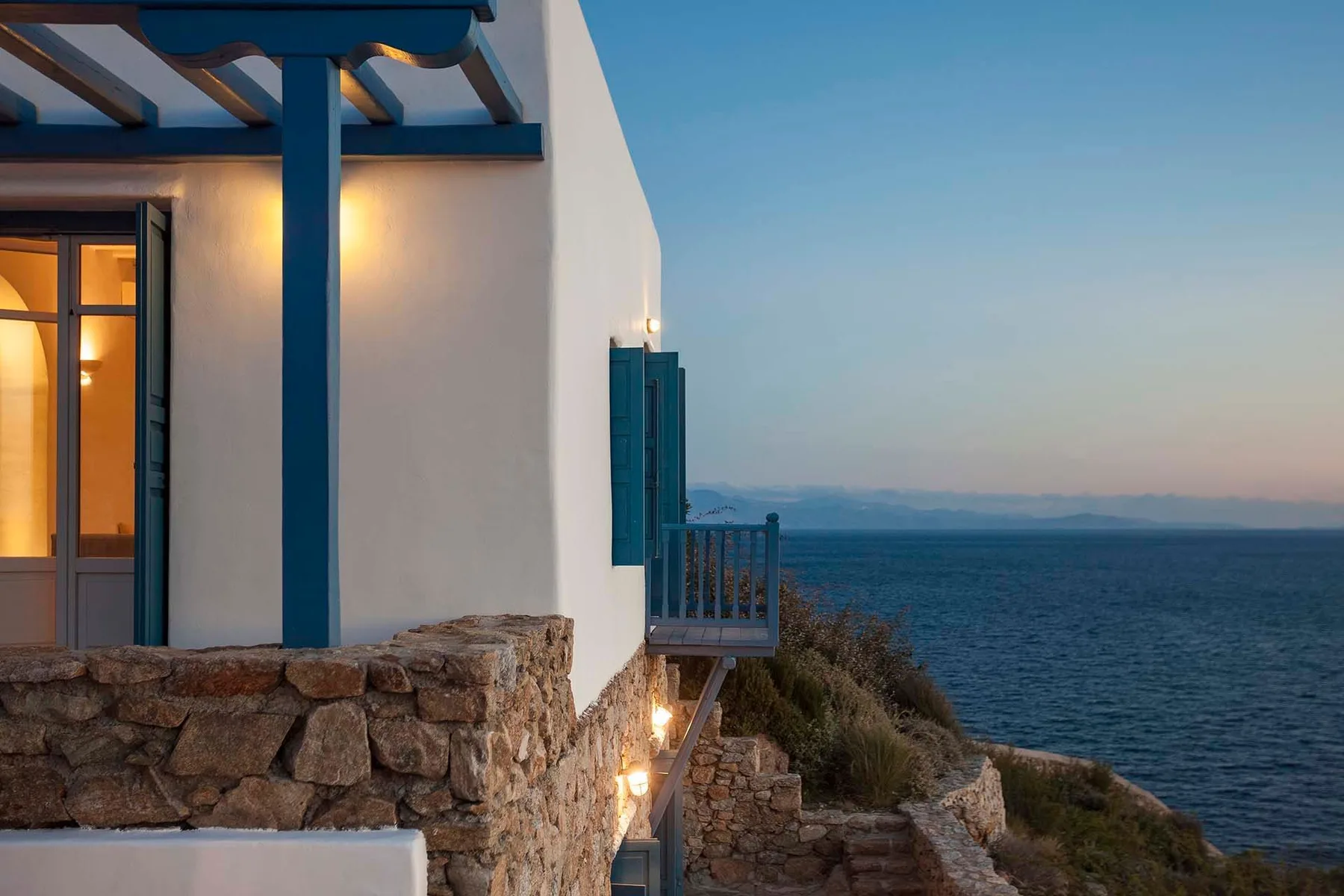 A white seaside building with a lit window overlooks the water.