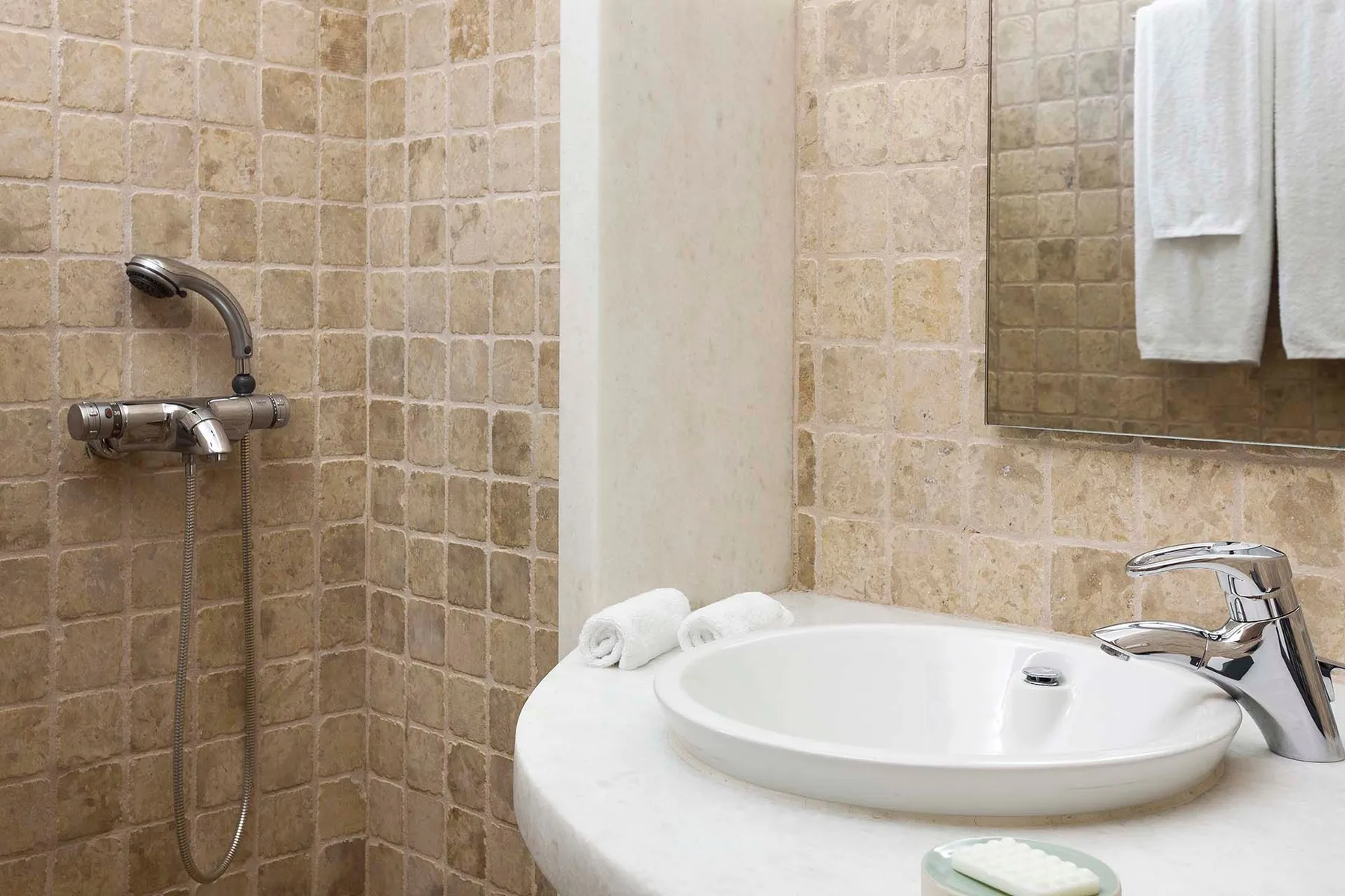 A tiled bathroom vanity with a round basin, wall-mounted shower, and towels.