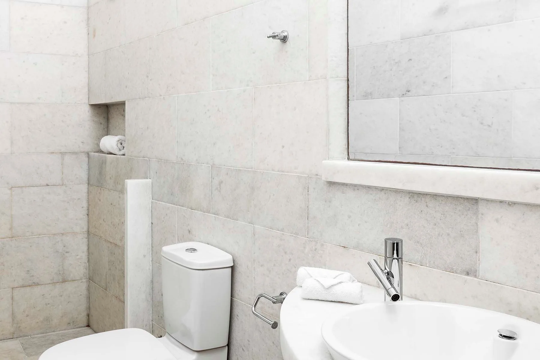 A tiled bathroom with a toilet, sink, and large wall mirror.