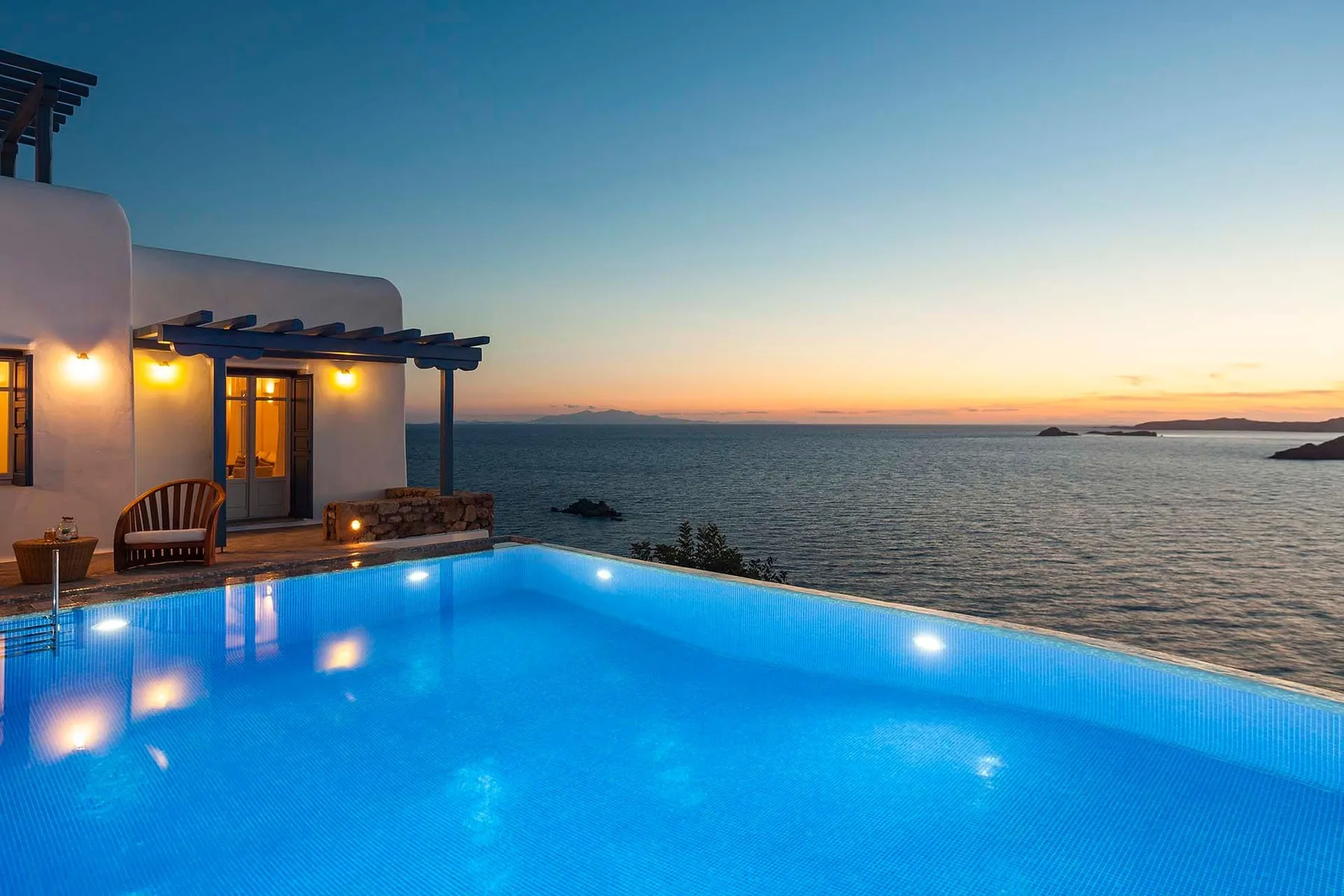 An illuminated swimming pool beside a seaside building at sunset.