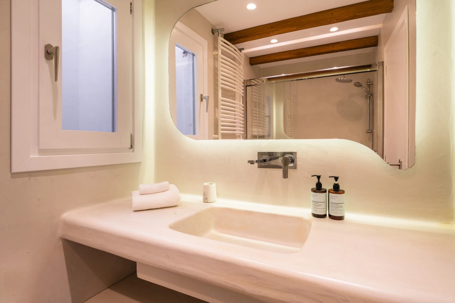 A bathroom vanity with a sink, wall mirror, and shower in the background.