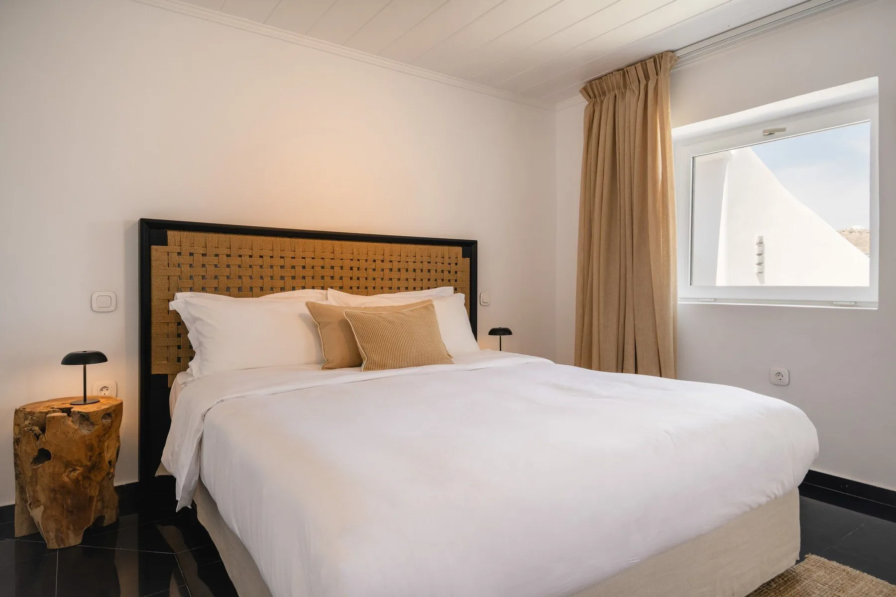 A bedroom with a neatly made bed and a window beside beige curtains.