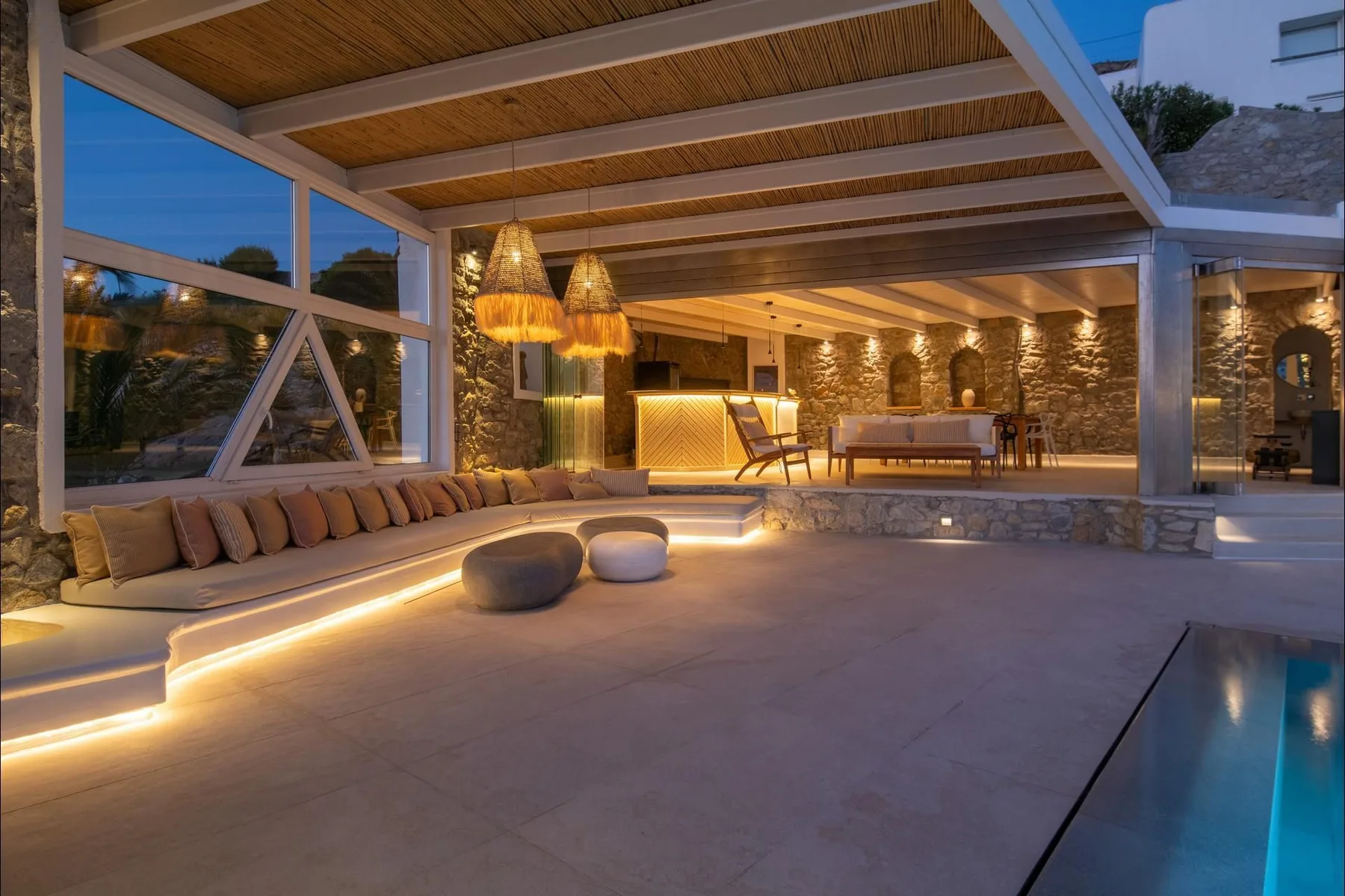 A covered outdoor lounge opens onto a swimming pool, with warm lighting and seating.
