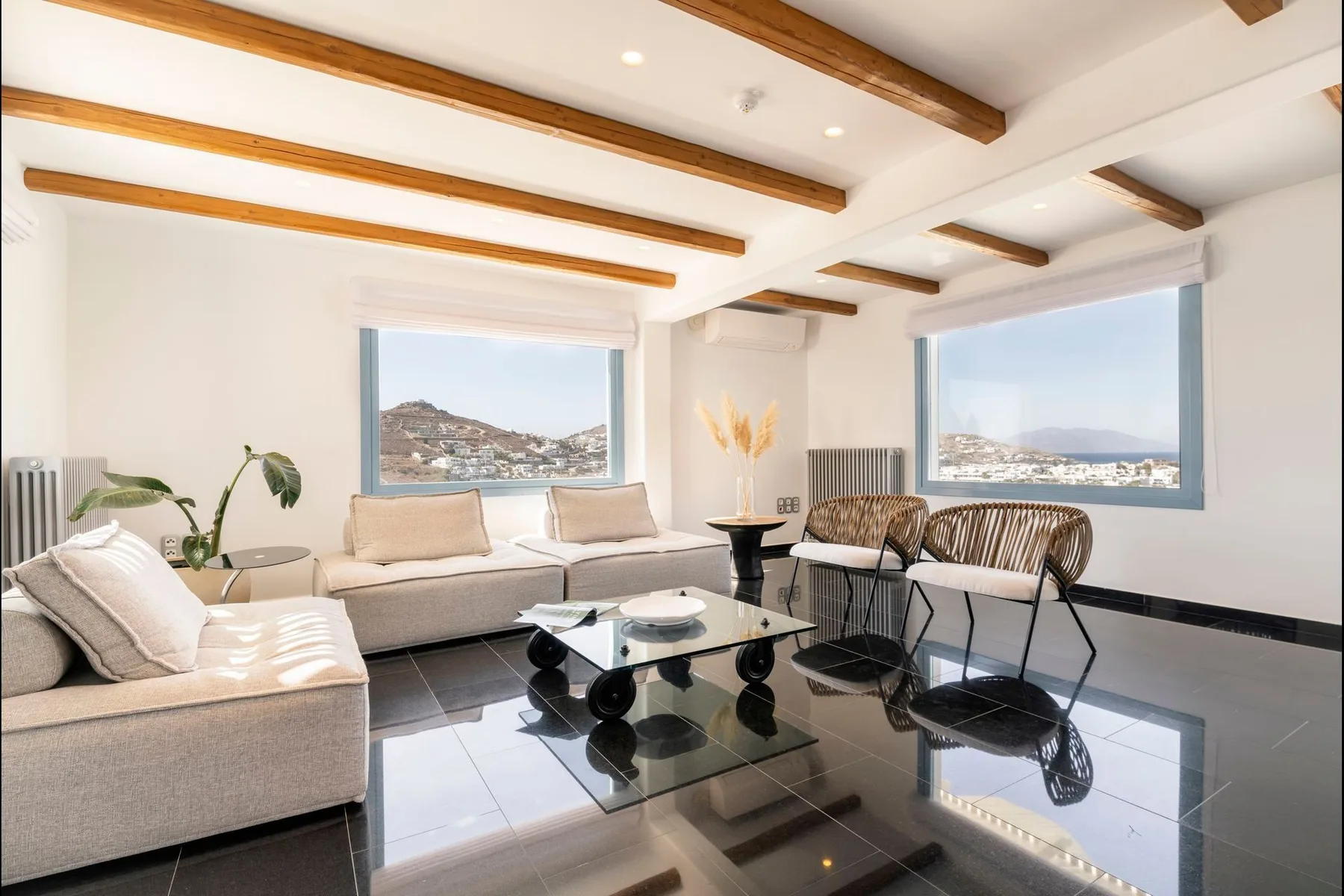 A bright living room with seating, glass tables, and large windows overlooking a hillside.