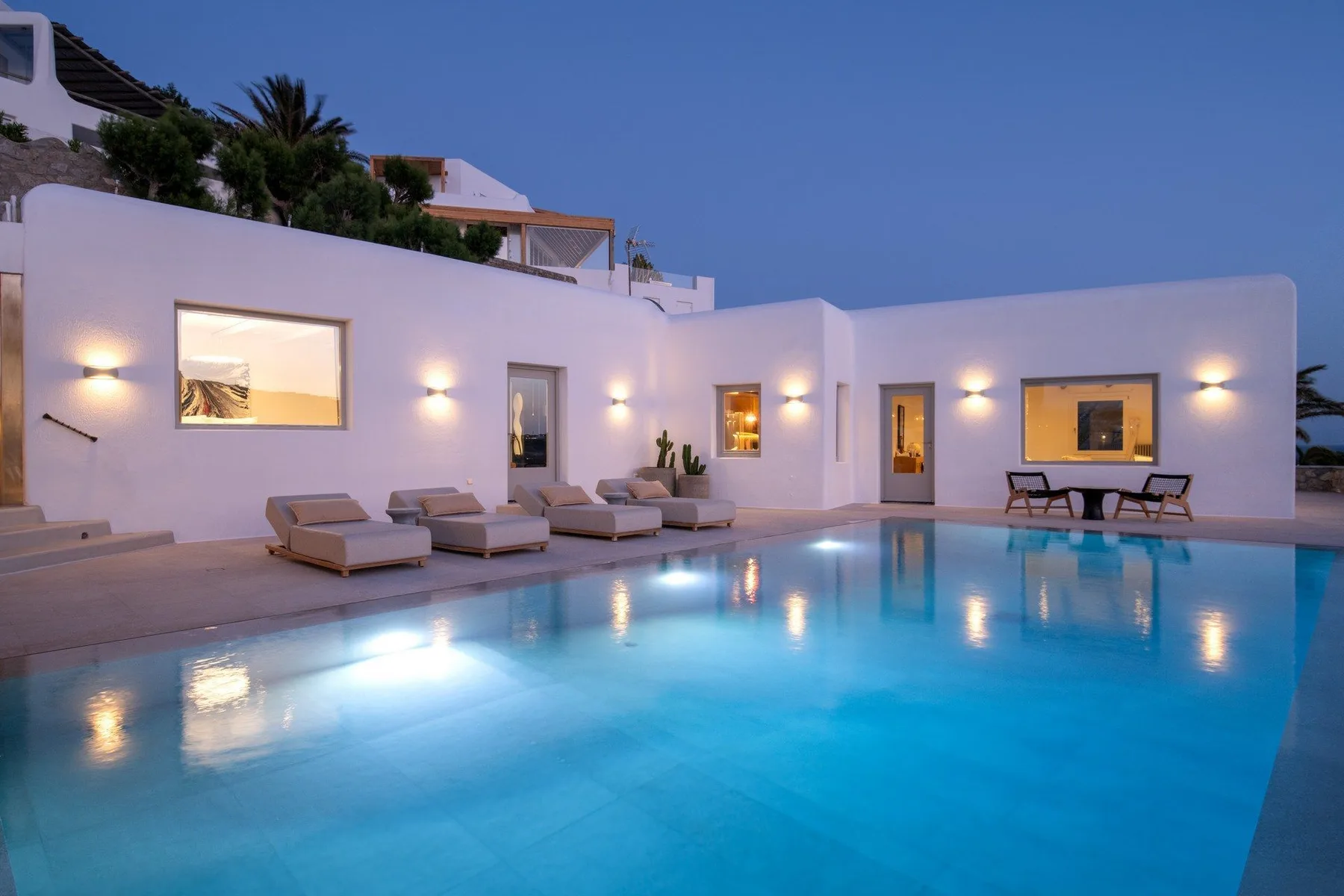 An outdoor swimming pool sits beside a white building with lit windows.