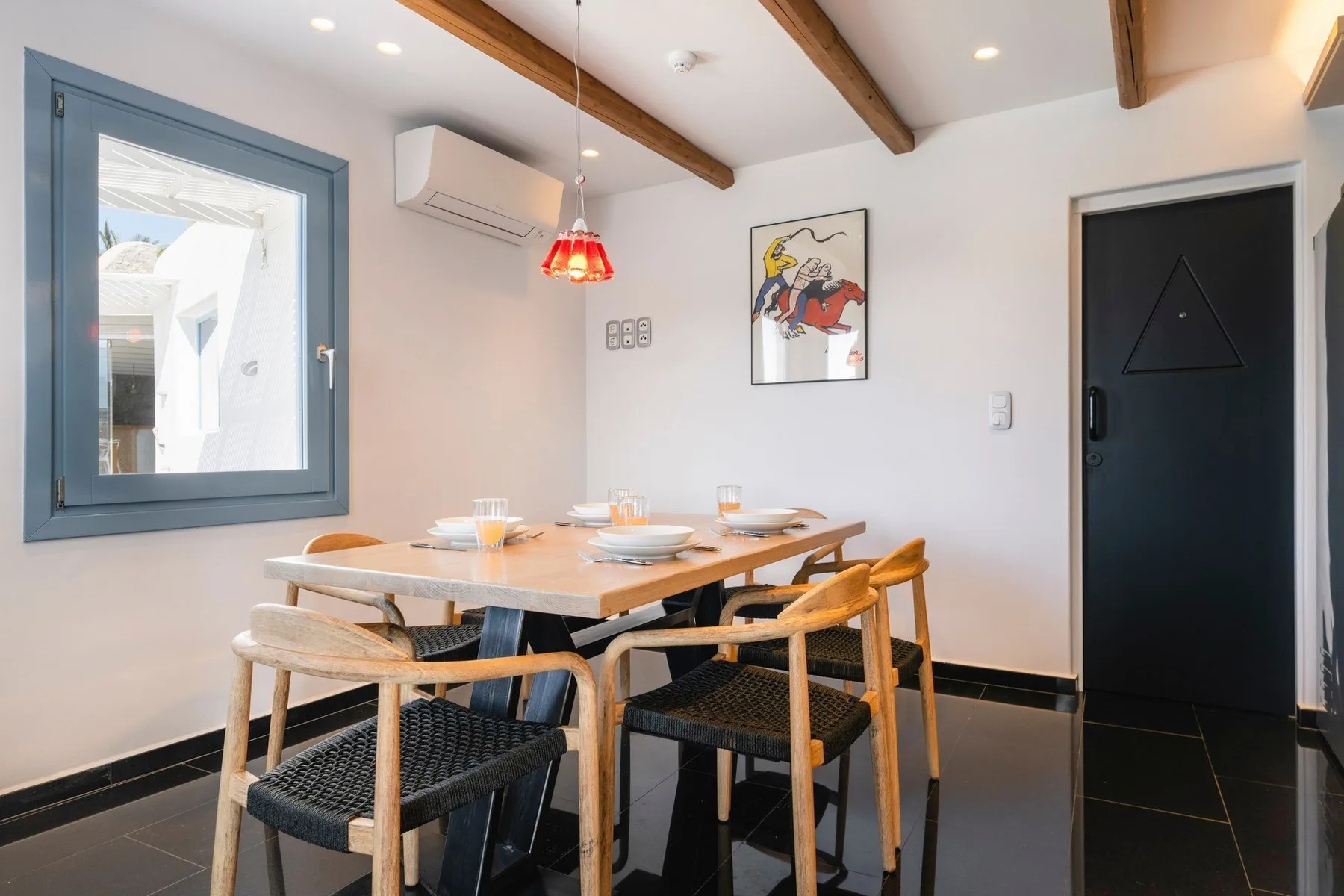 A dining area with a wooden table and woven-seat chairs beneath exposed ceiling beams.