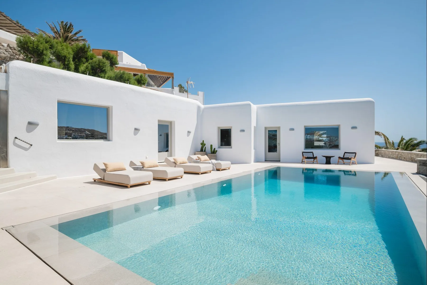 A bright white villa courtyard opens onto a swimming pool with sun loungers.