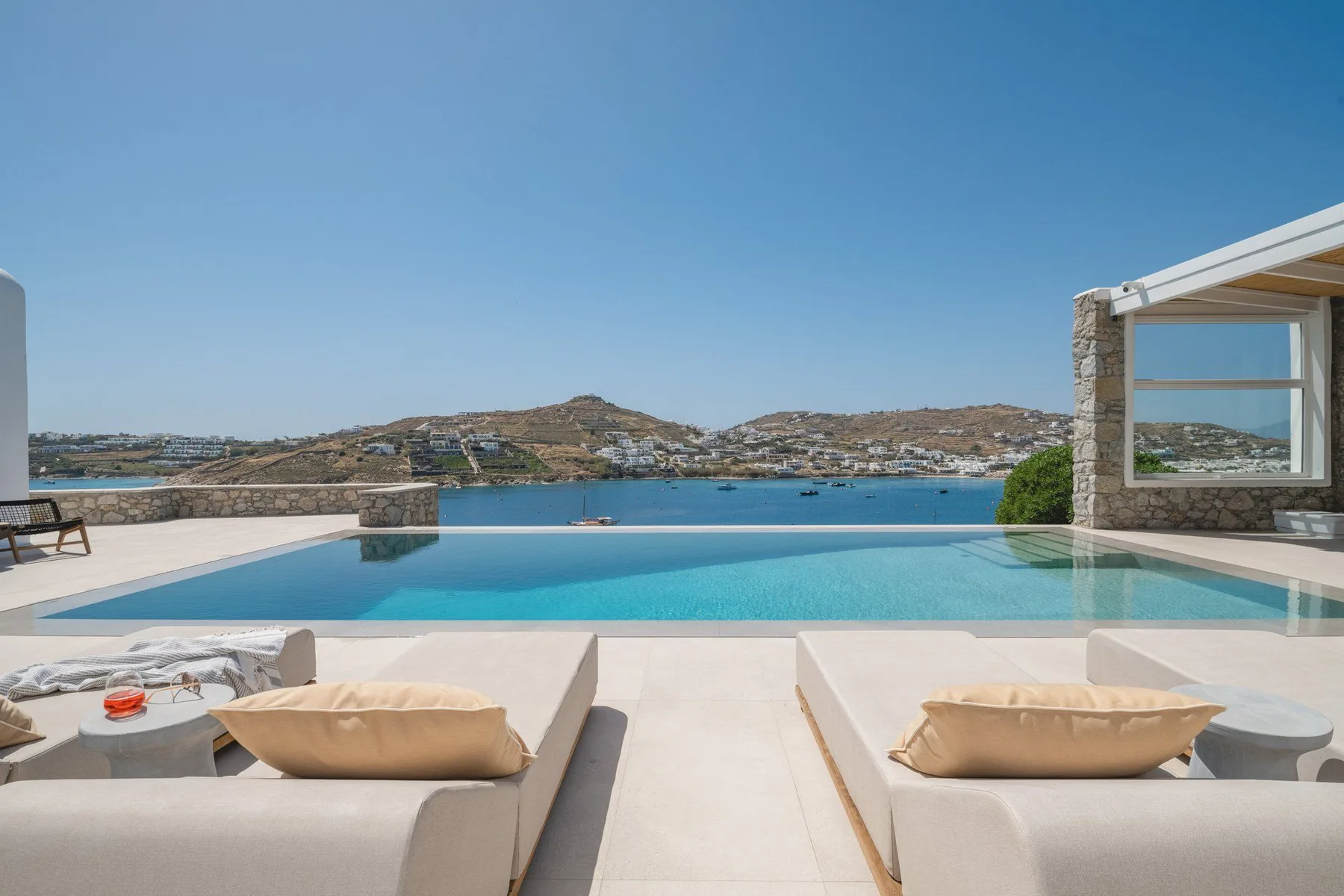 An outdoor swimming pool overlooks the sea, with lounge seating in the foreground.