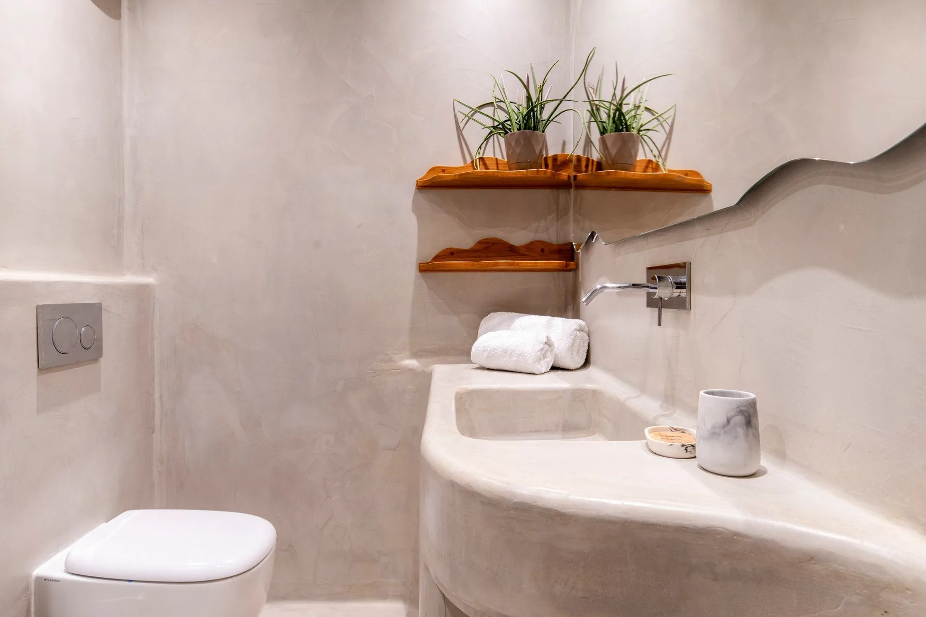 A bathroom with a toilet, sink, and plants on wall shelves.