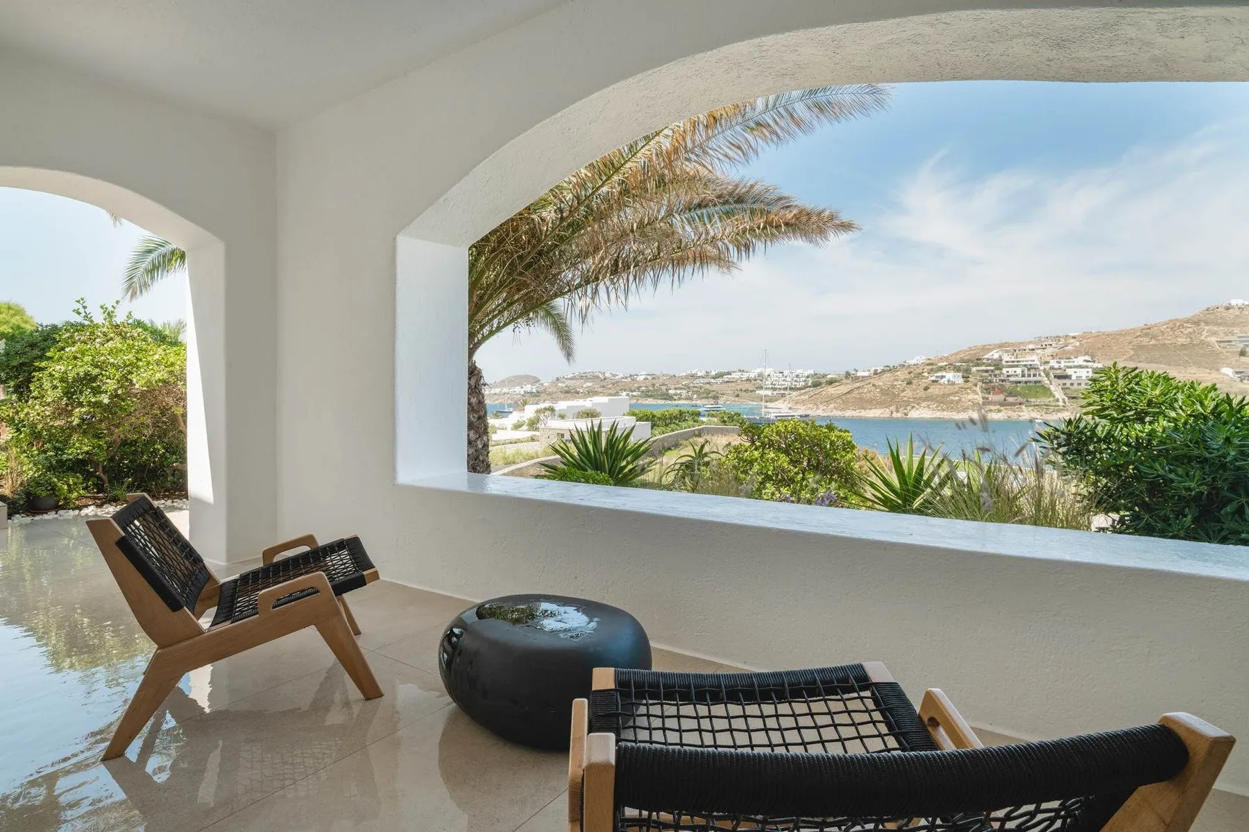 A covered terrace with lounge seating overlooks water and a hilly shoreline.