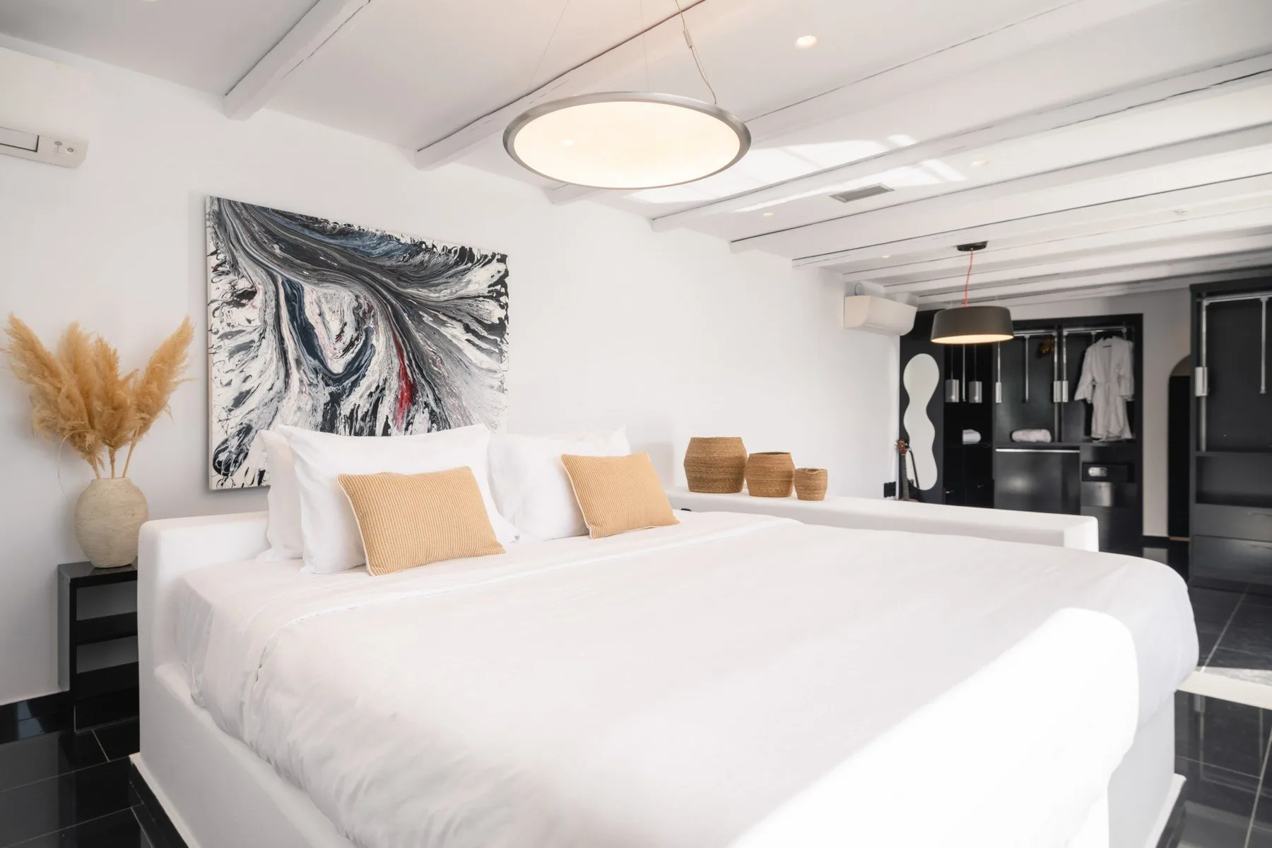 A bedroom with a large white bed, neutral pillows, and abstract wall art.