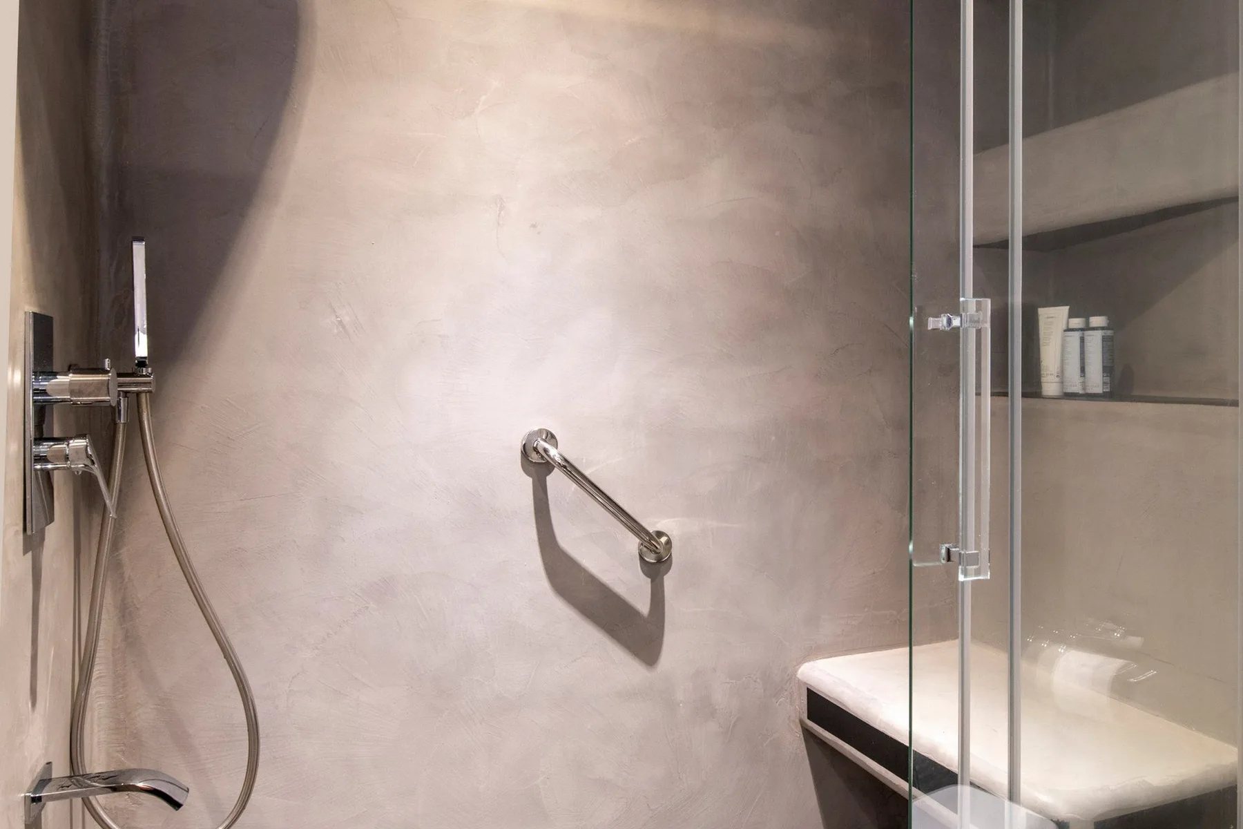 A bathroom shower area with a grab bar and a glass partition.
