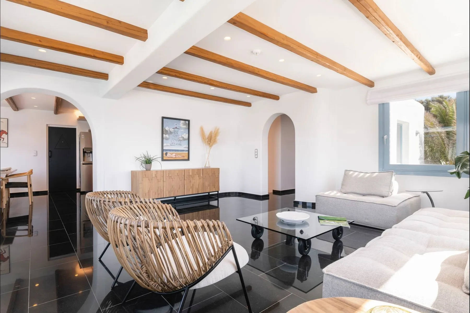 Bright living room with seating around a glass coffee table and exposed ceiling beams.