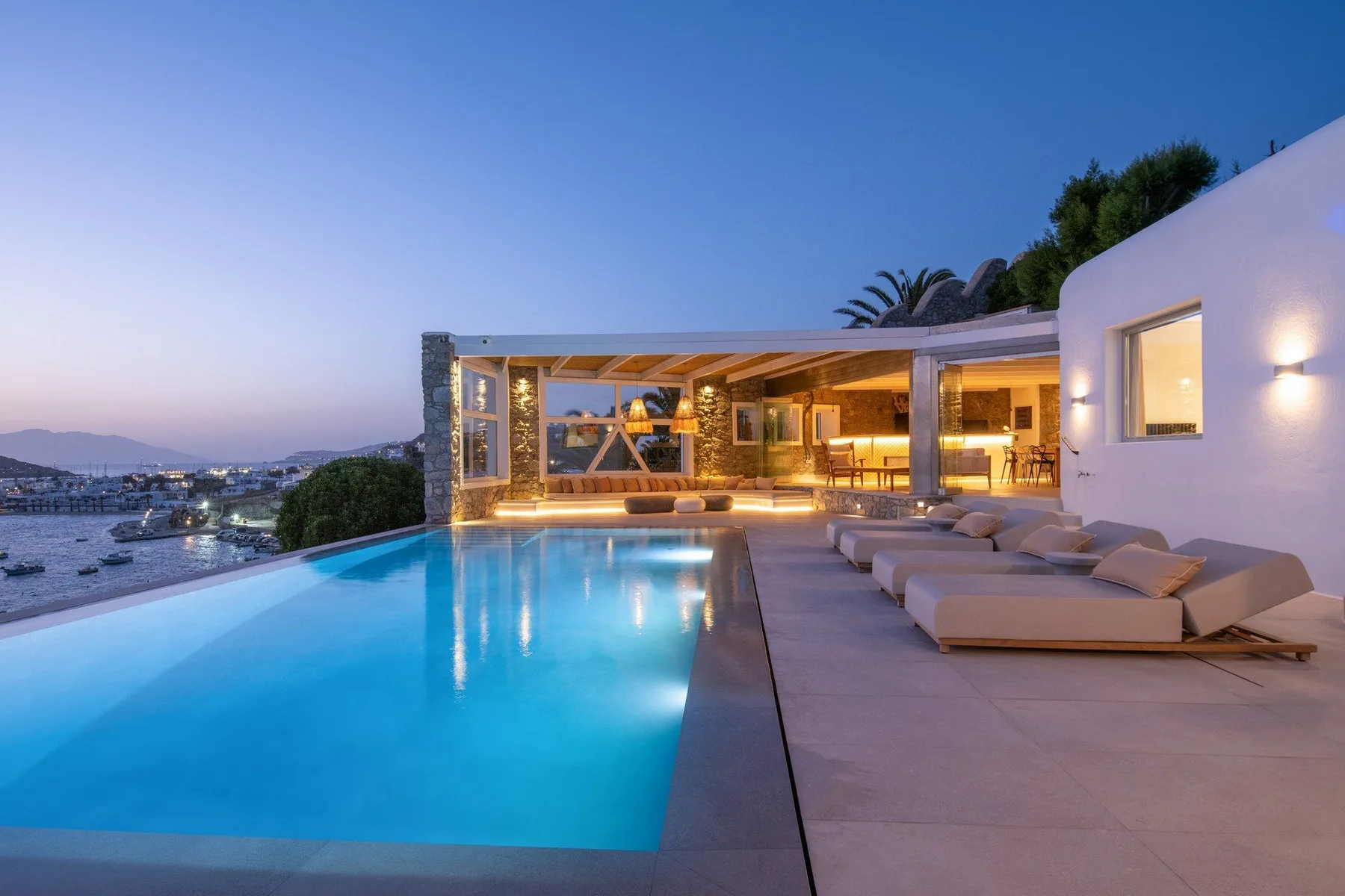 An outdoor pool beside a modern house, with lounge seating and a coastal view.