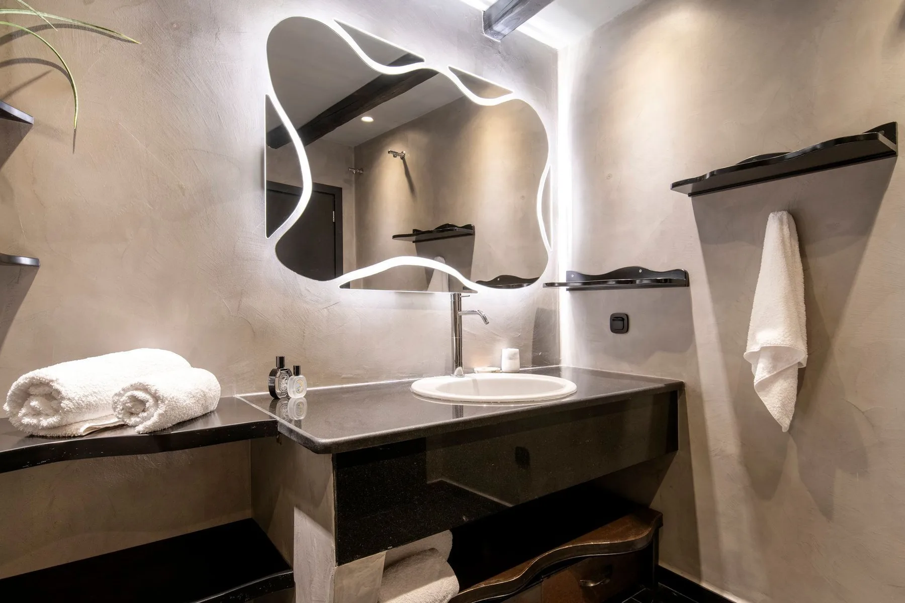 A bathroom vanity with a sink sits beneath a large illuminated mirror.
