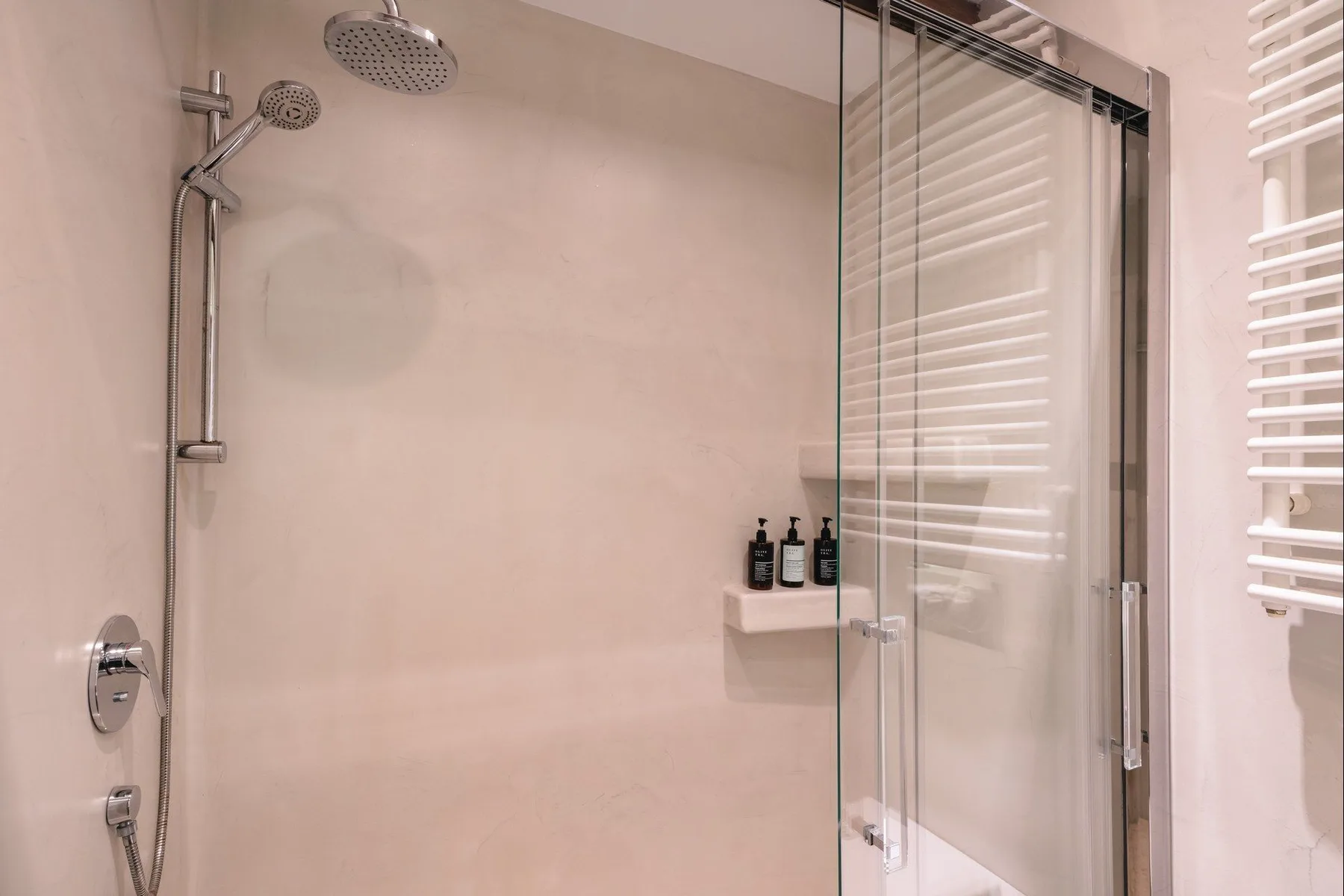 A bathroom shower with a handheld showerhead and glass panels.