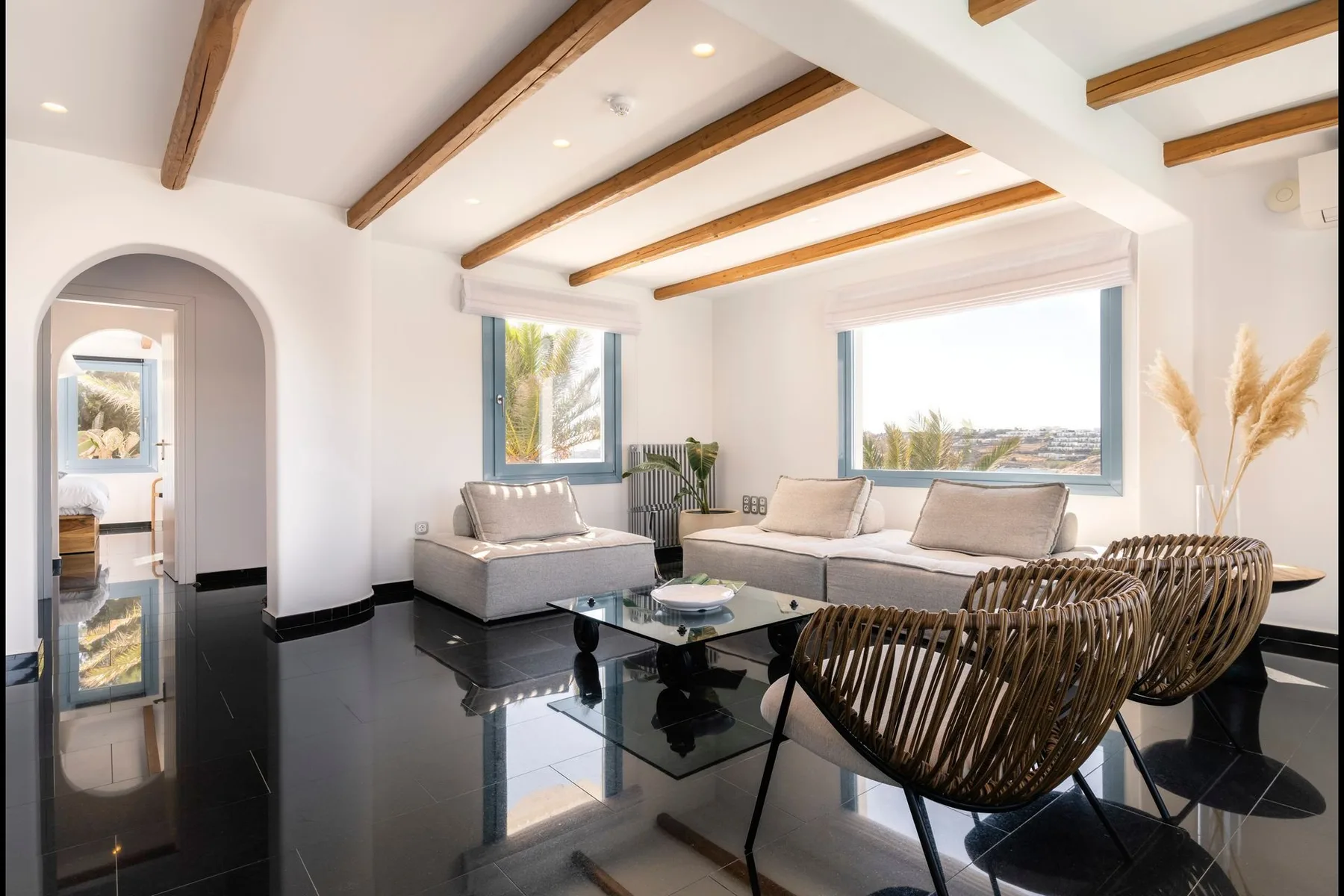 A bright living room with seating, a glass coffee table, and exposed ceiling beams.