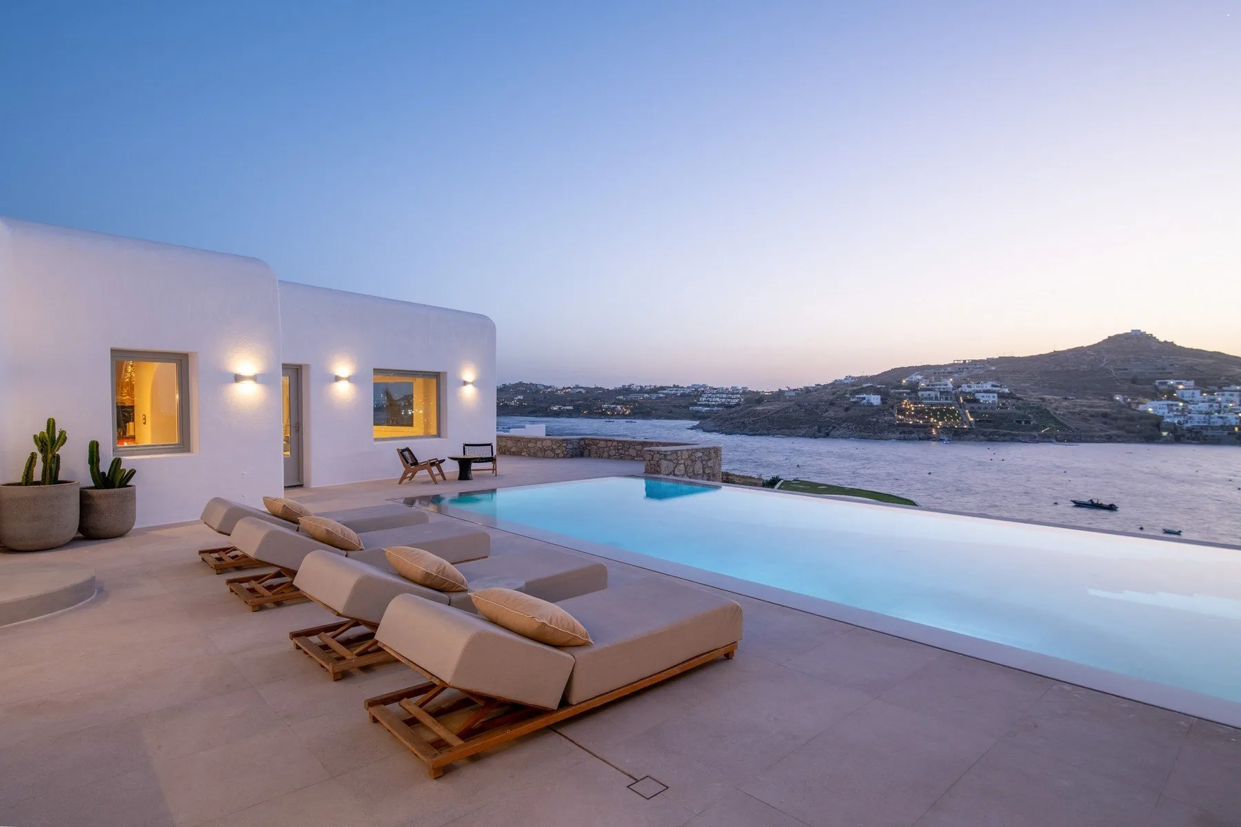 A terrace with lounge seating overlooks a swimming pool and distant coastal hills.
