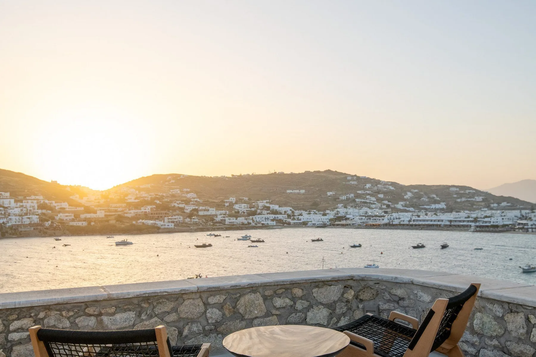 A waterfront terrace overlooks a bay with boats at sunset.