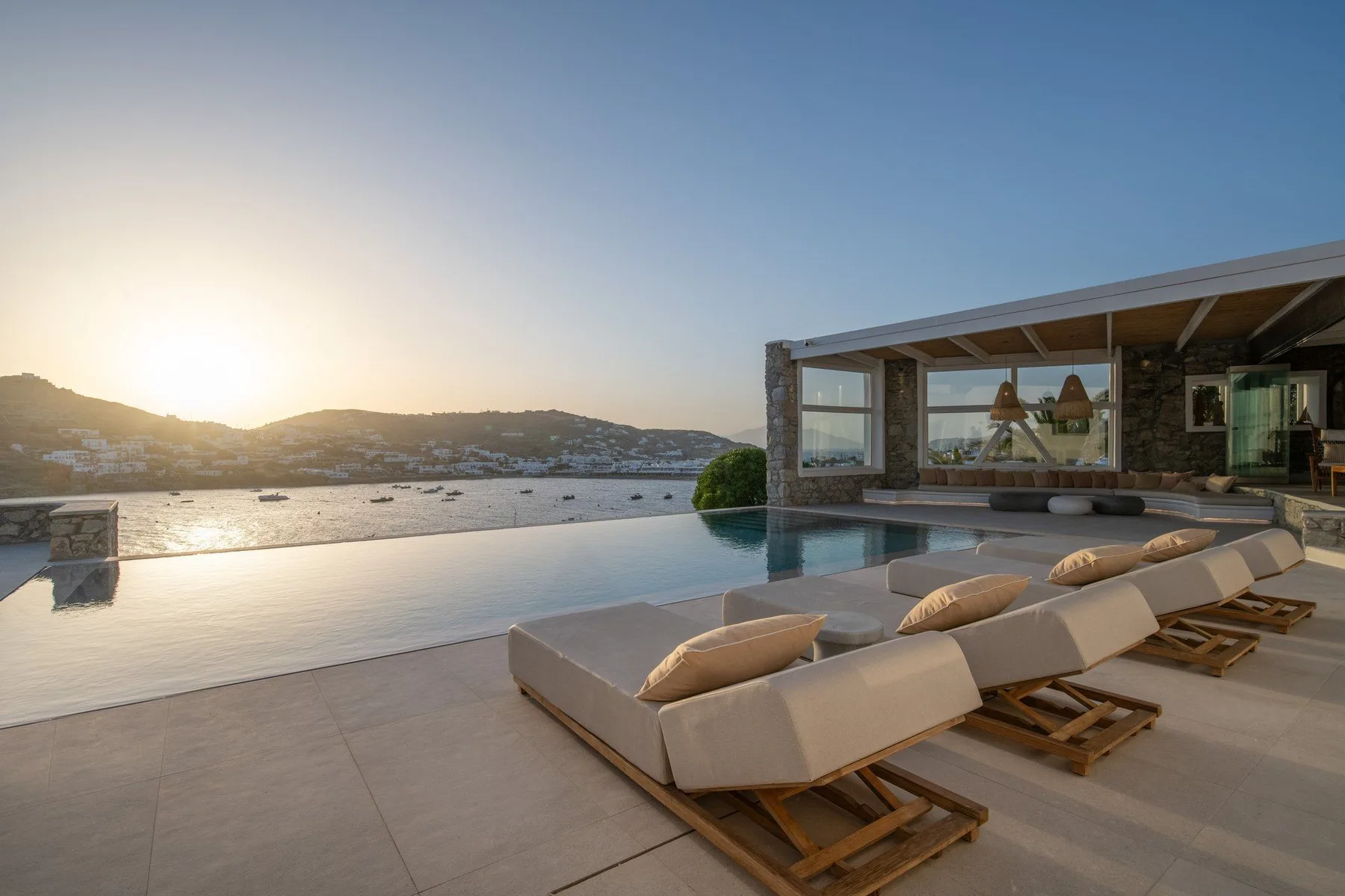 An outdoor pool and loungers overlook the water at sunset.