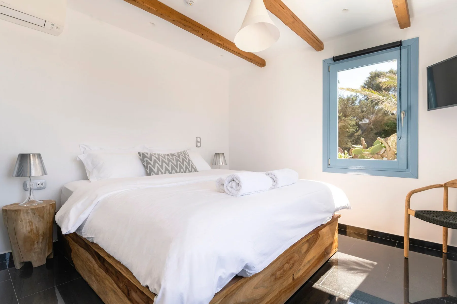 A bedroom with a neatly made bed and a window overlooking greenery.