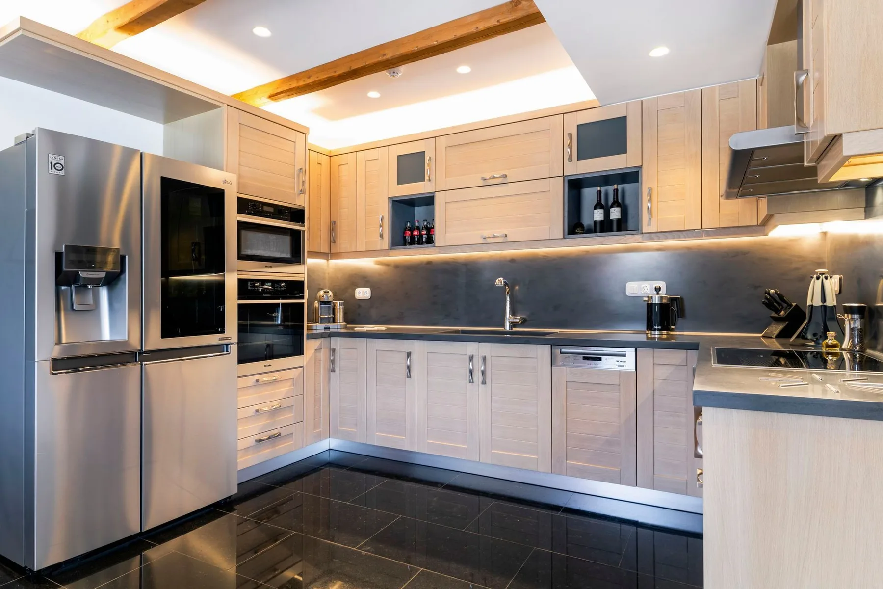 A modern kitchen with light wood cabinetry, dark countertops, and stainless steel appliances.