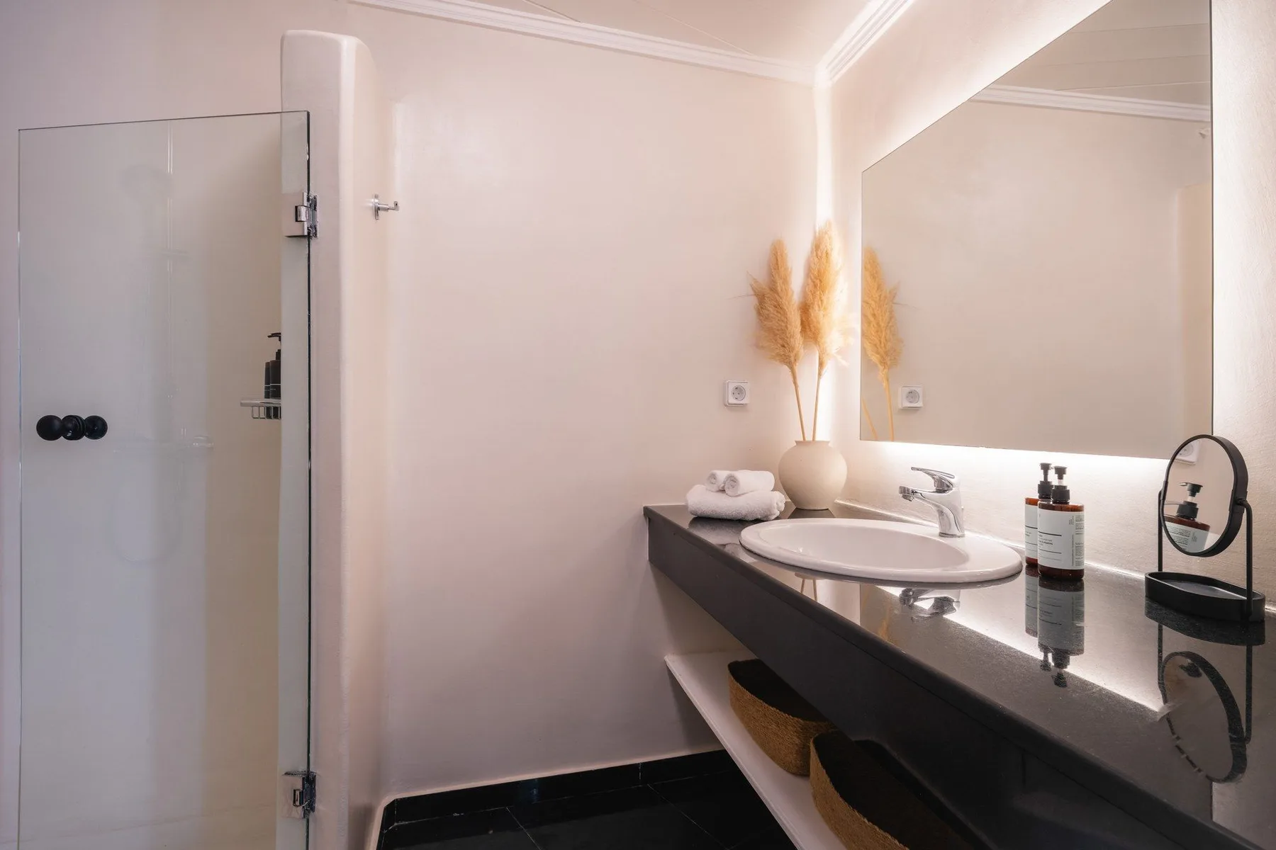 A bathroom with a glass shower, sink, and large wall mirror.
