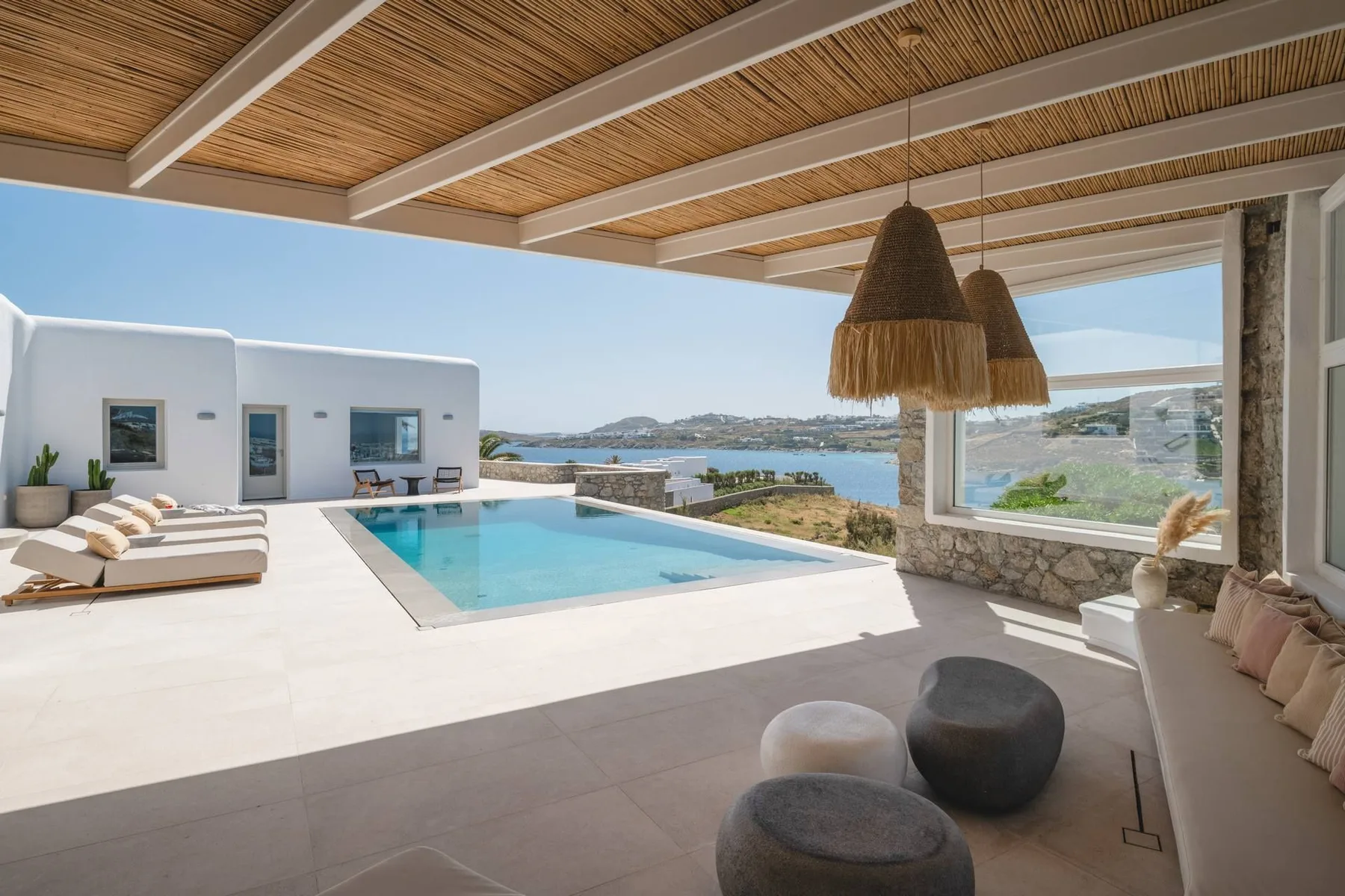 A covered outdoor lounge overlooks a swimming pool and the sea.