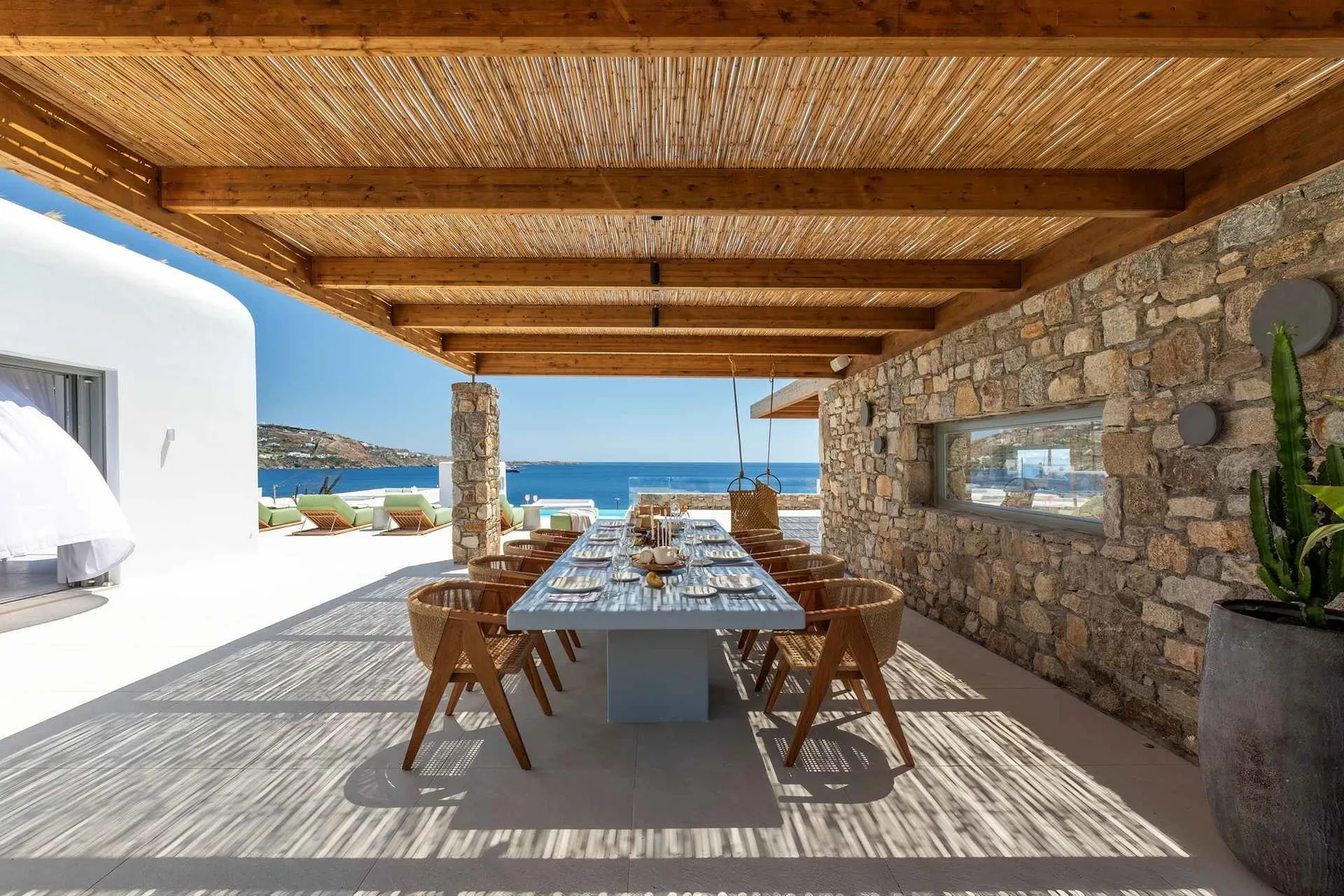 A covered outdoor dining area has a long table facing the sea.