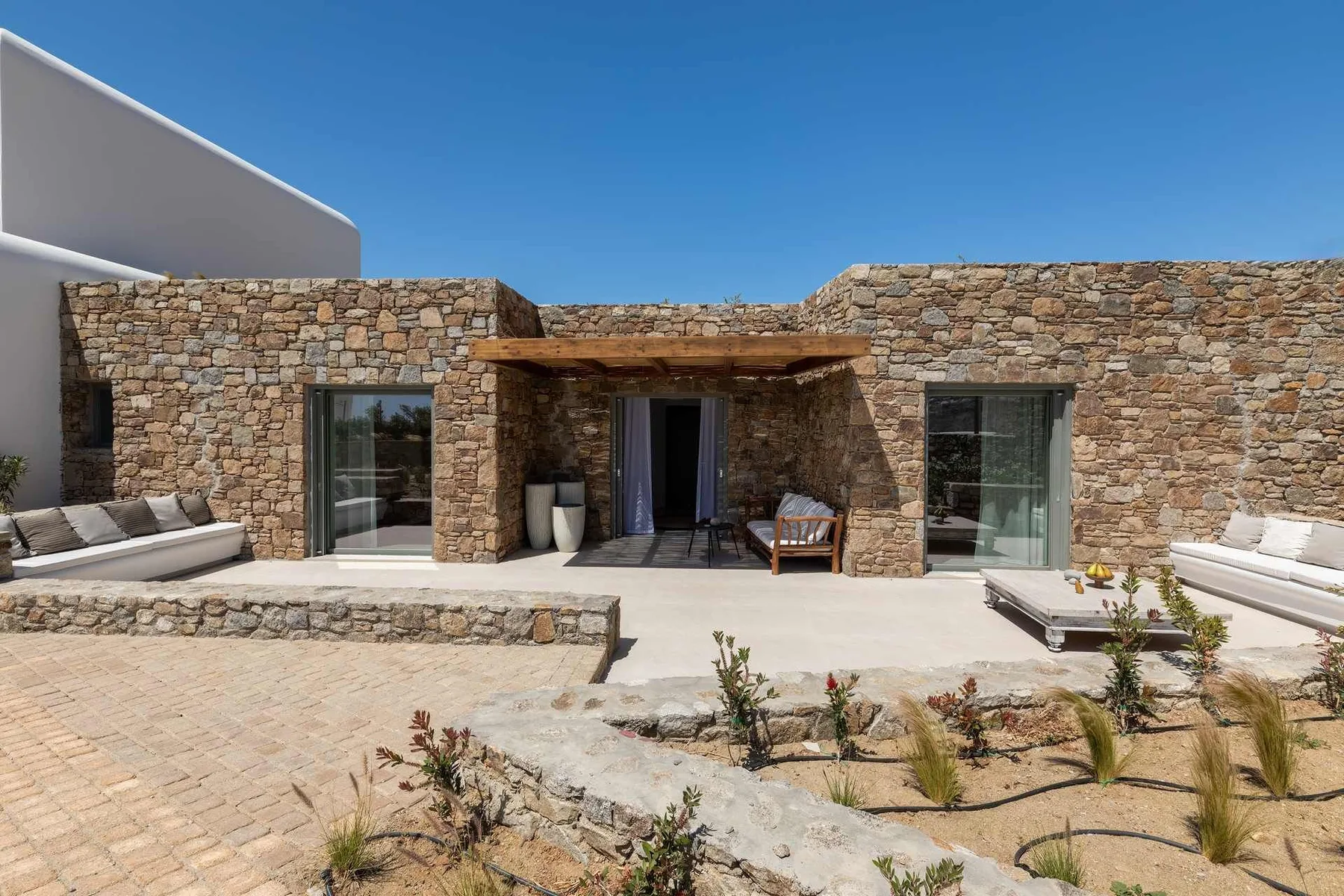 A stone courtyard patio with outdoor seating and glass doors beneath a wooden awning.