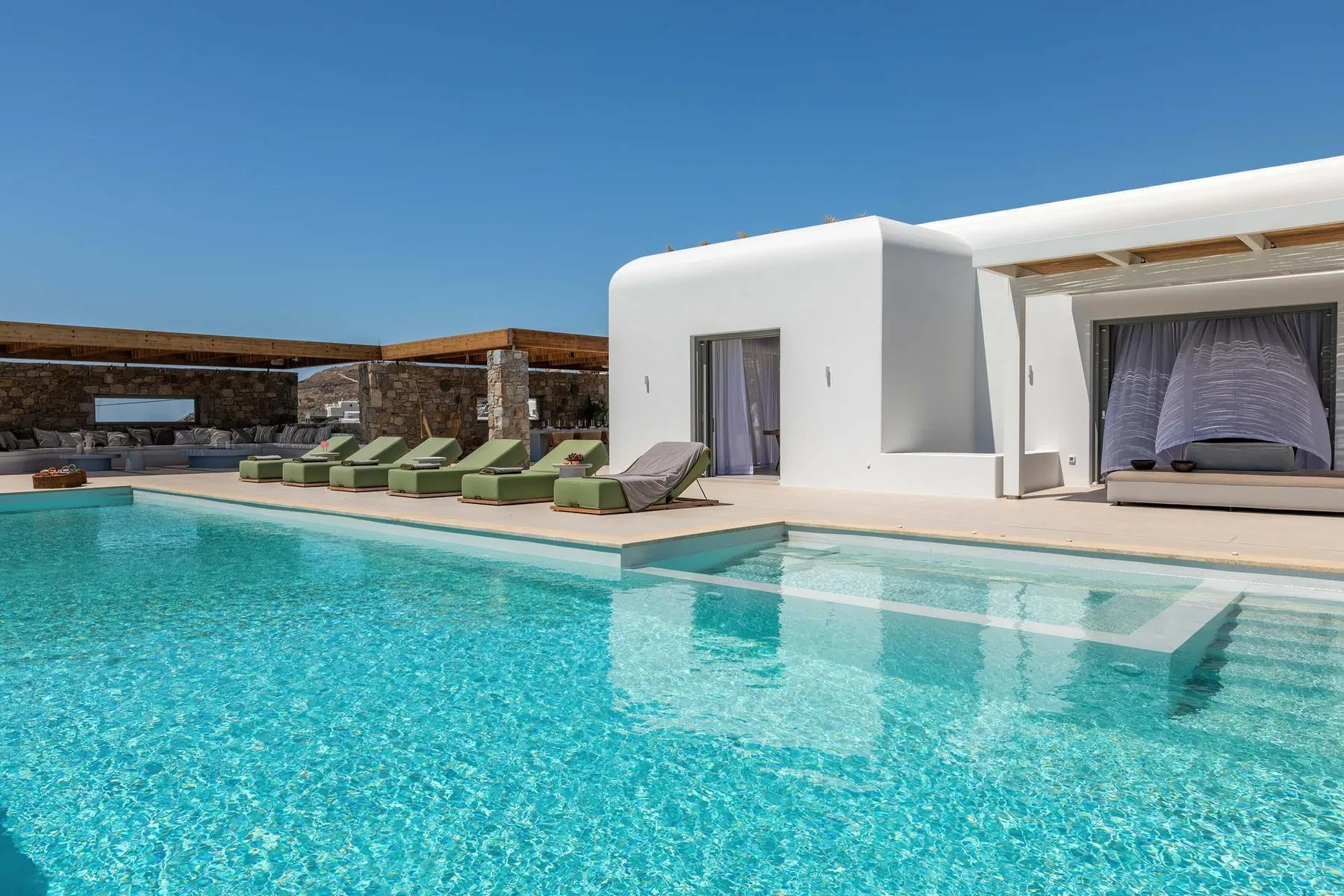 A swimming pool beside a white building, with lounge seating along the edge.